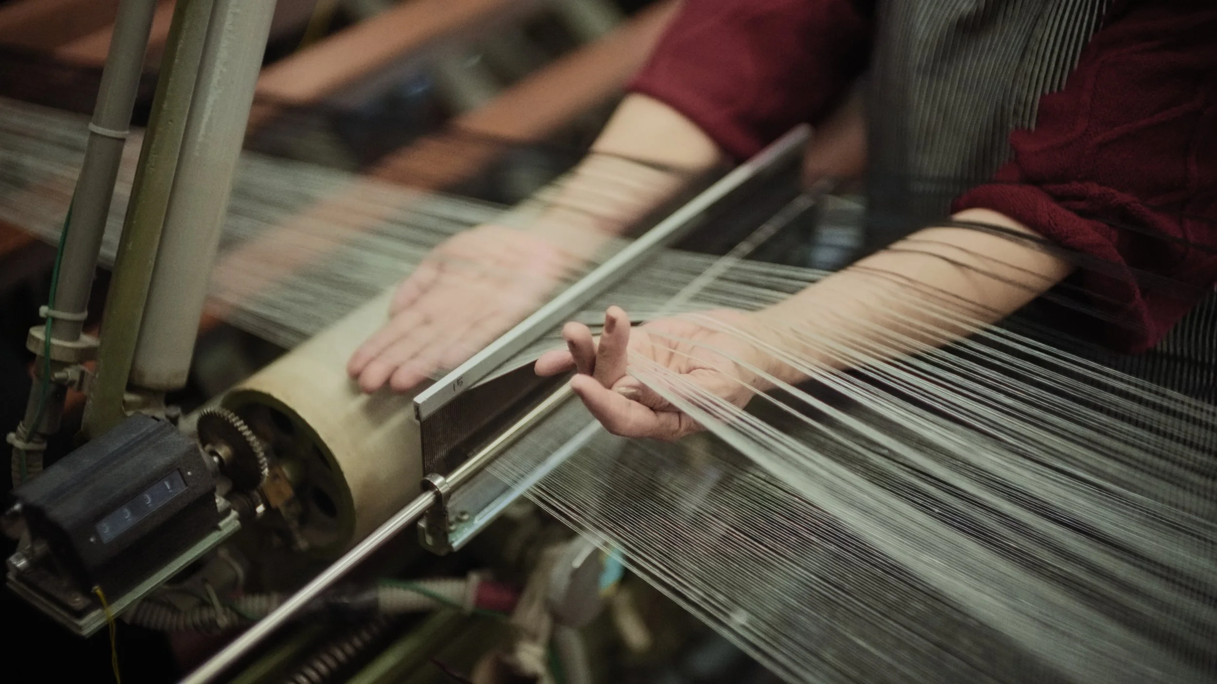 Close-up of a traditional loom weaving fabric, with a person's hand holding and guiding the warp threads.
