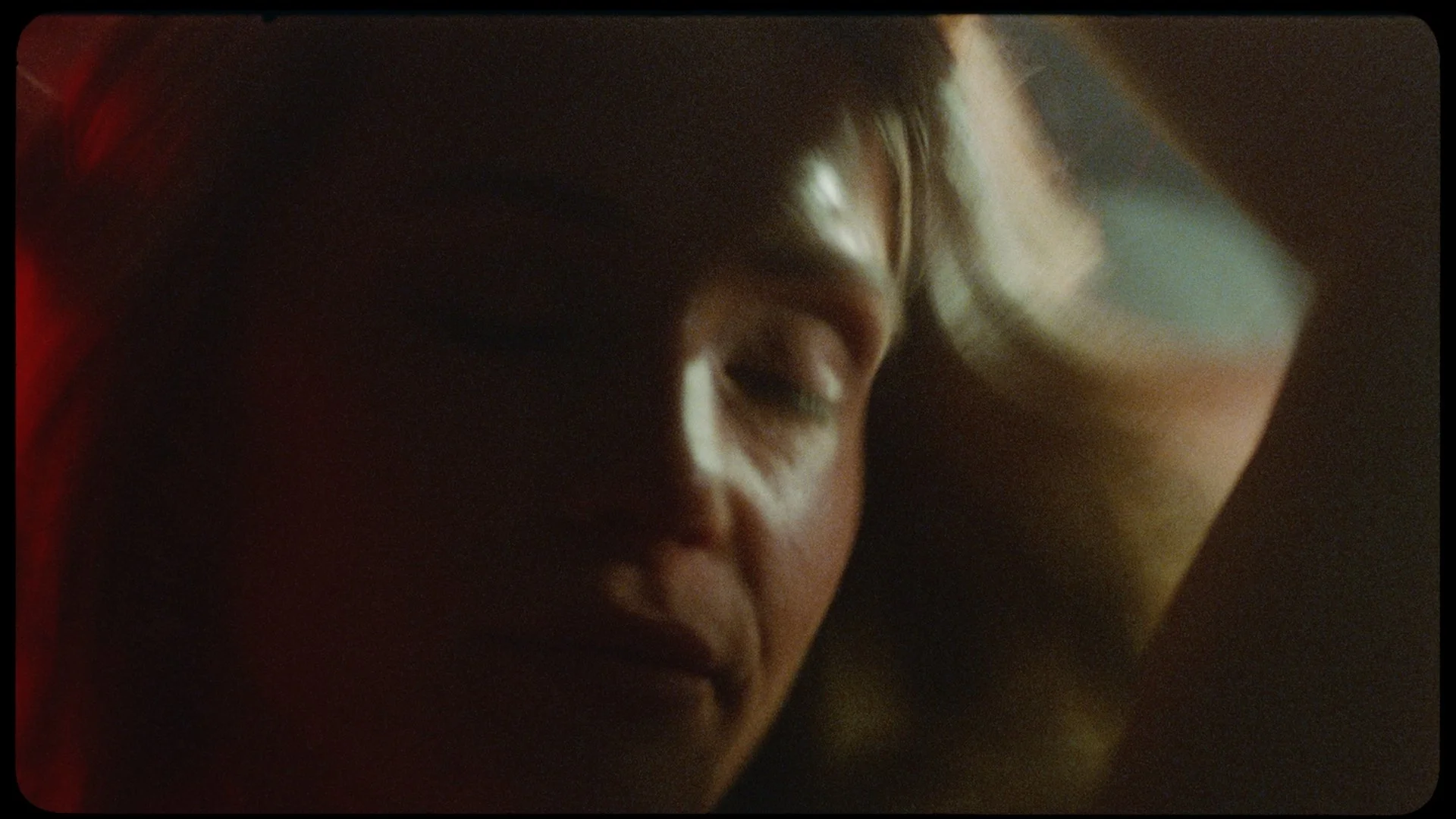 A person lying in bed with closed eyes, resting their head on a pillow in a dimly lit room.