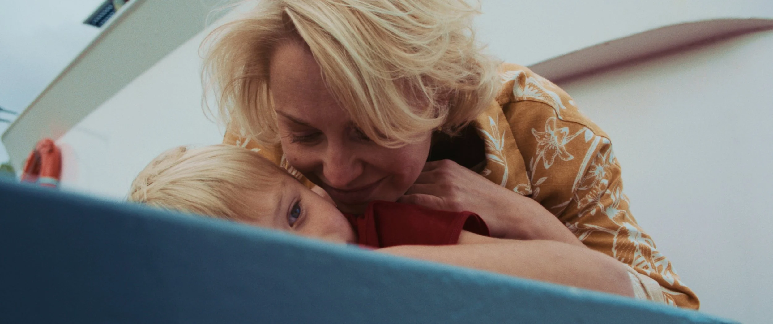 A woman with blonde hair embracing a young blonde boy with blue eyes on a hospital bed.
