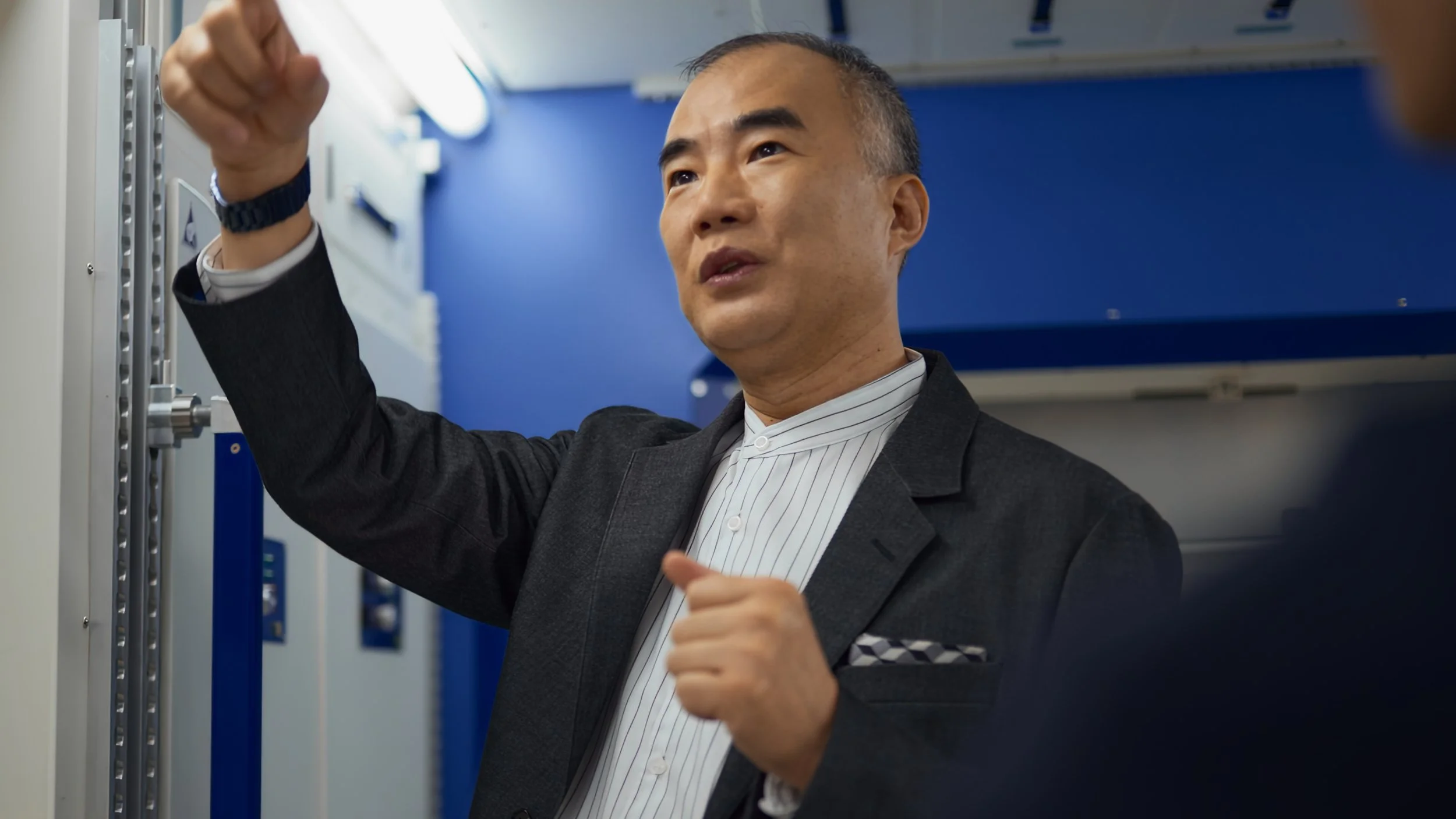 A man in a suit inspecting electrical panels in a technical or industrial setting.
