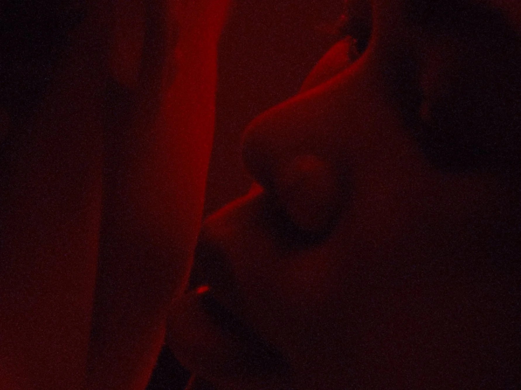 Dark image with faint red light illuminating some shapes, possibly fabric or clothing, with details mostly obscured.
