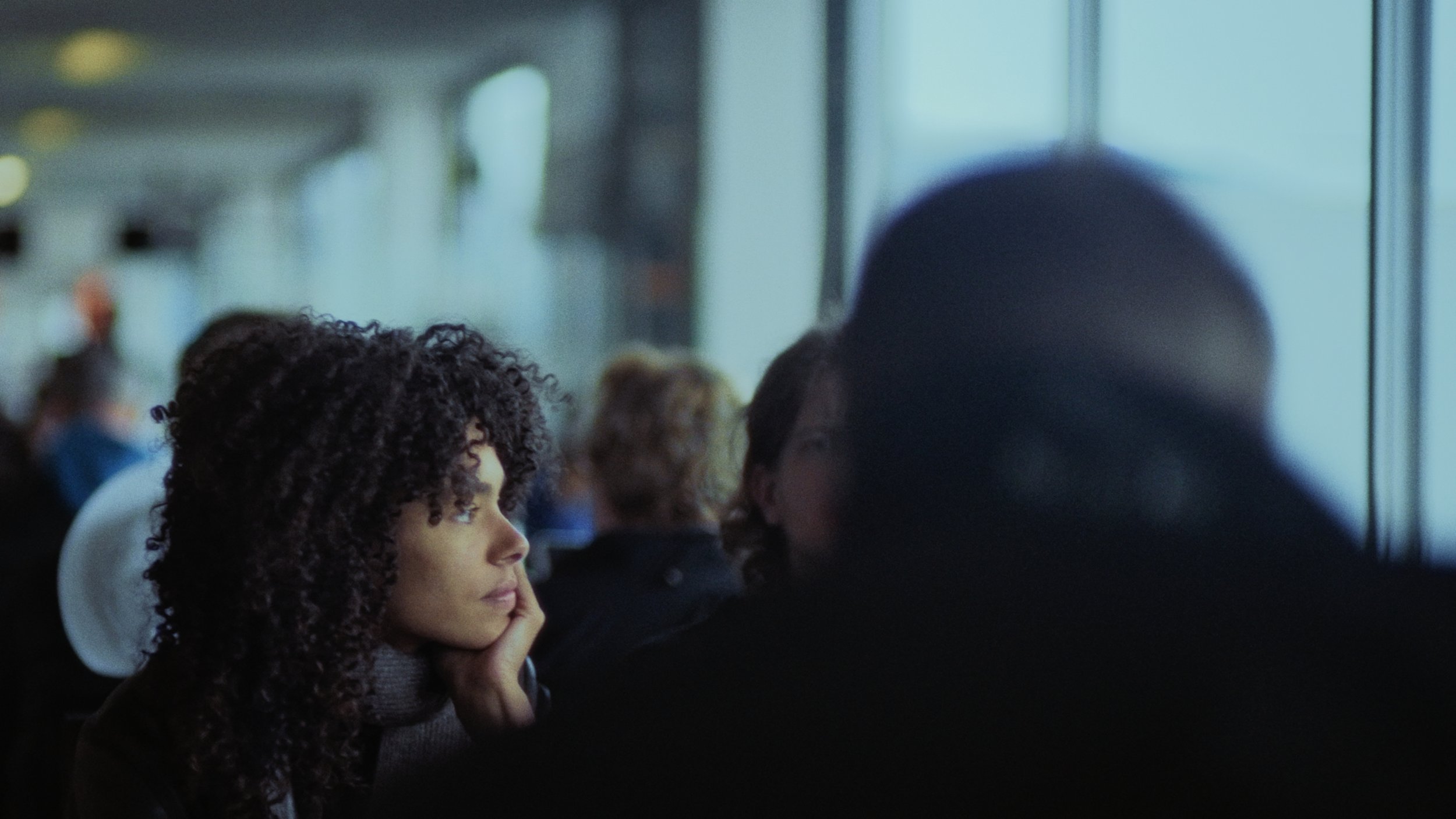 A woman and a young girl with curly hair sitting together and looking out of a window inside a train or bus.