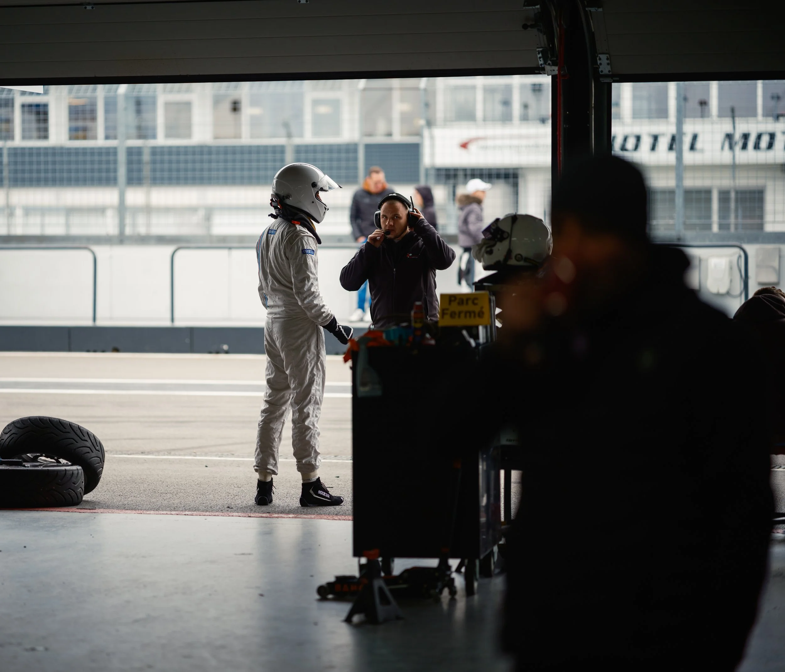 Race car garage with crew members preparing for a race, view from inside the garage showing team members and racing gear.
