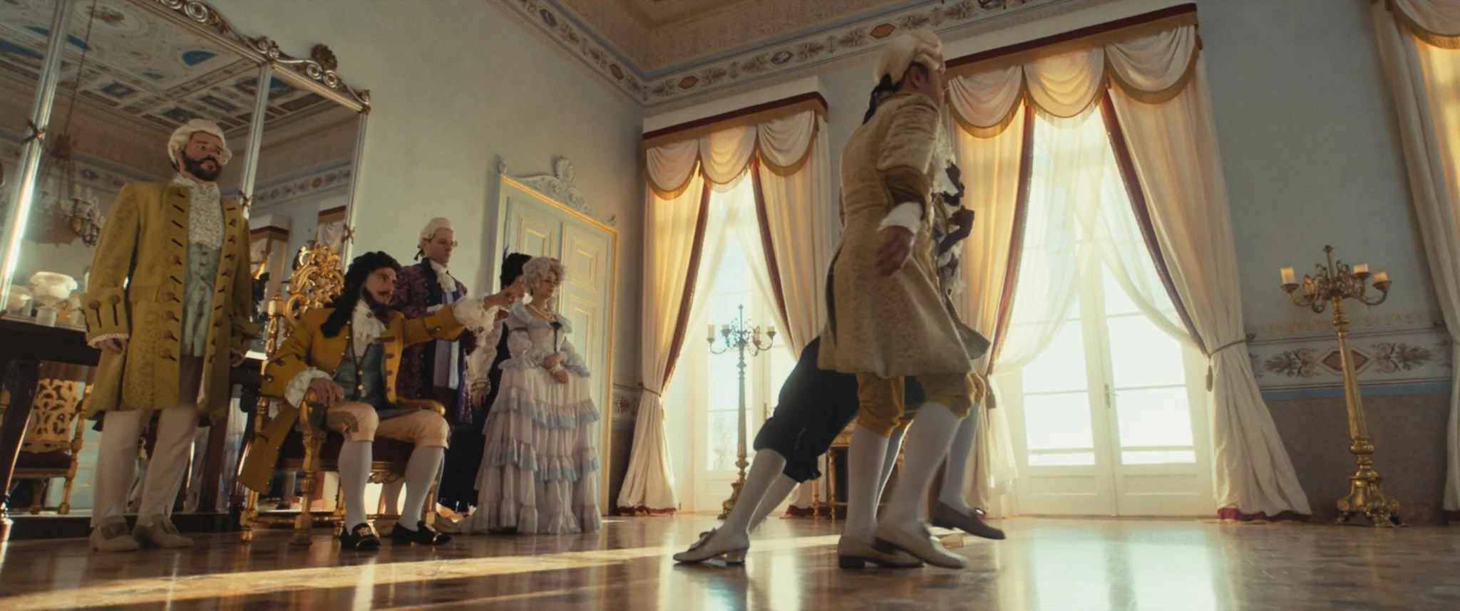 People in 18th-century costumes performing a dance in an ornate room with large windows and gold and cream curtains.