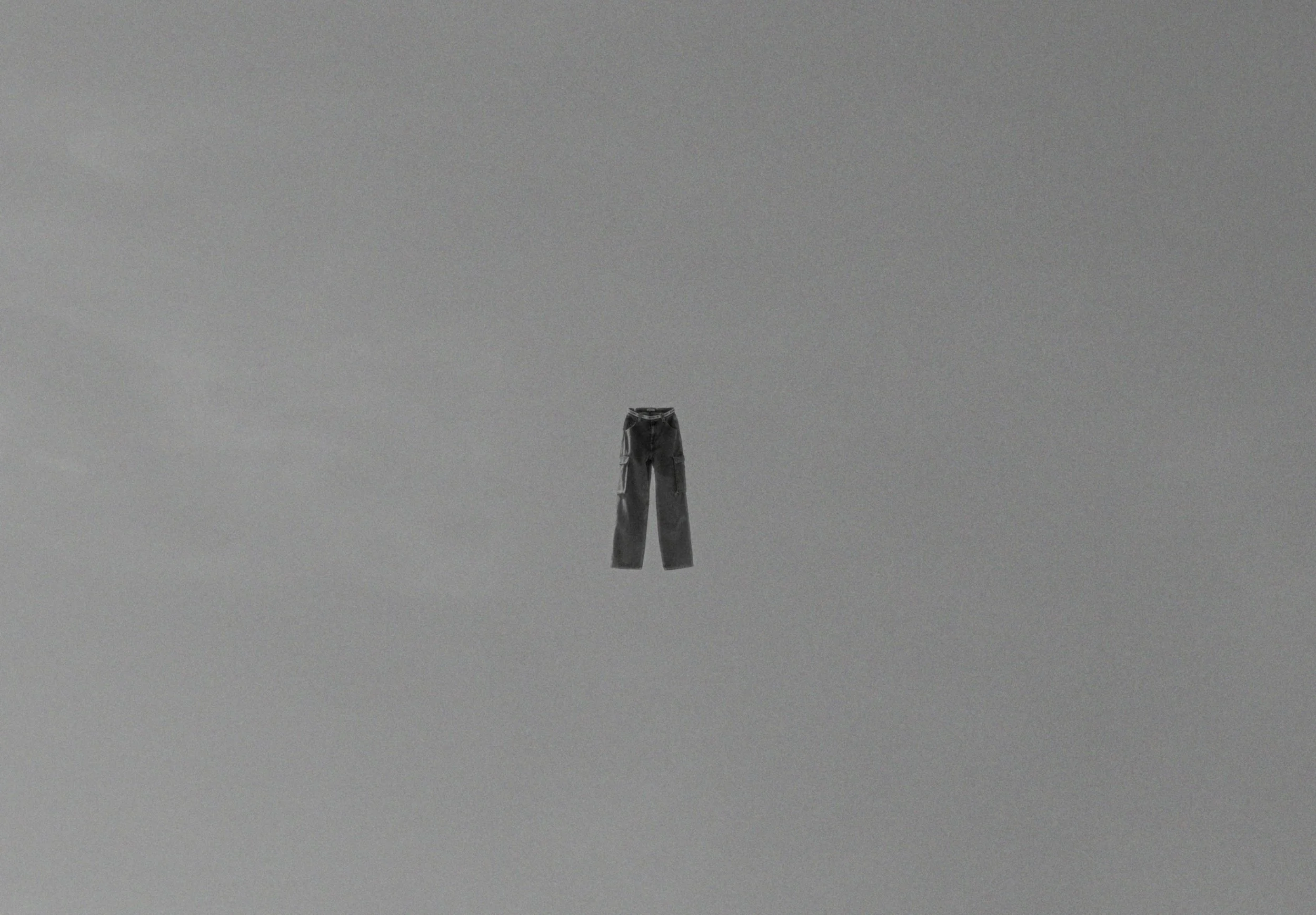 A pair of dark gray pants hanging in the center of a plain gray background.