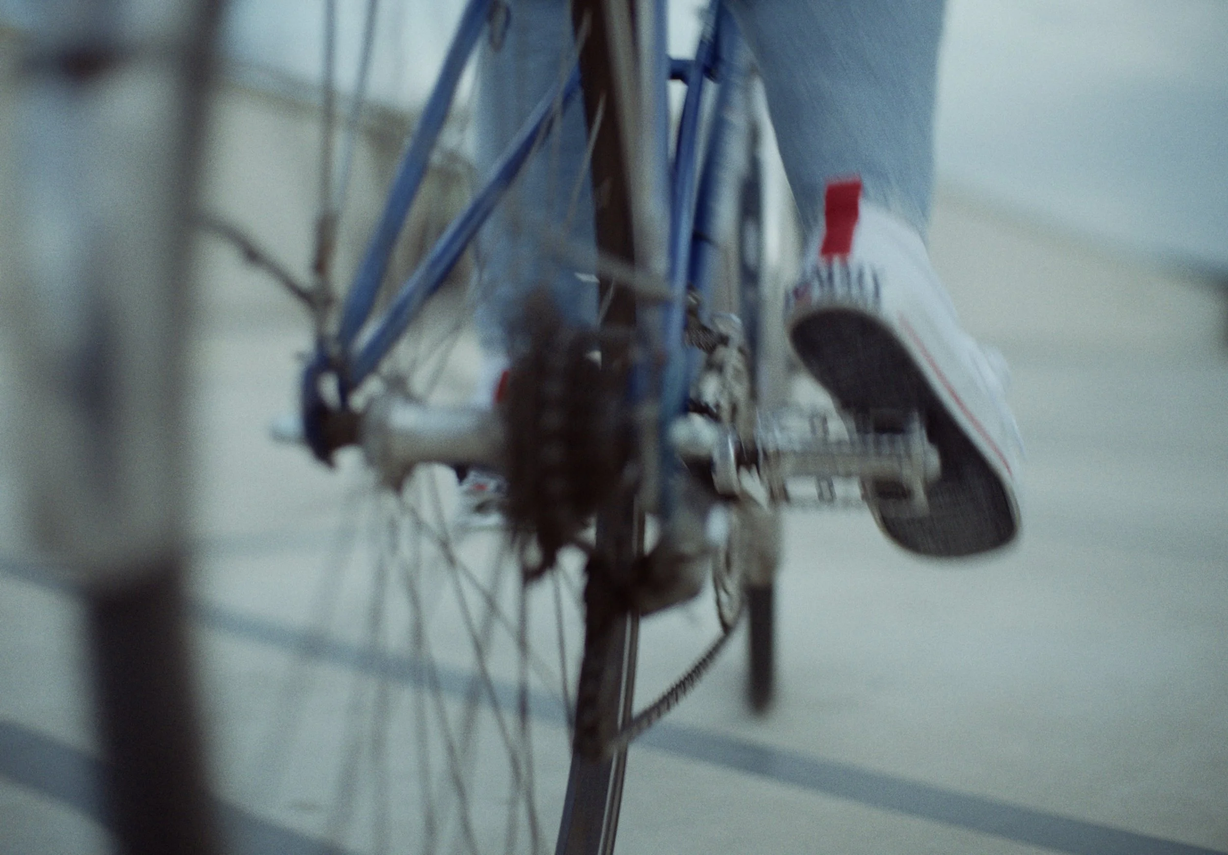 Close-up of a wheelchair, focusing on the wheels and frame, with a person's legs and sneakers visible in the background.