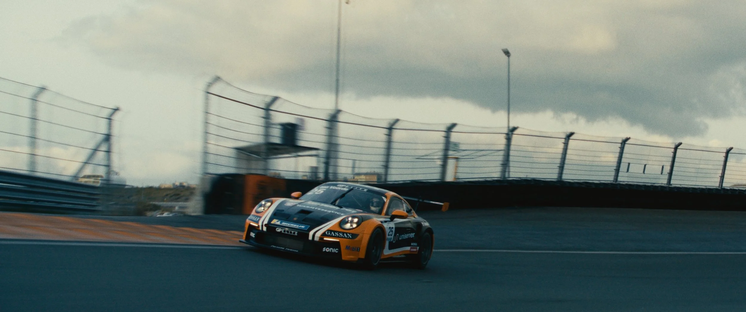 A racing car on a track with overcast skies and barriers along the side.