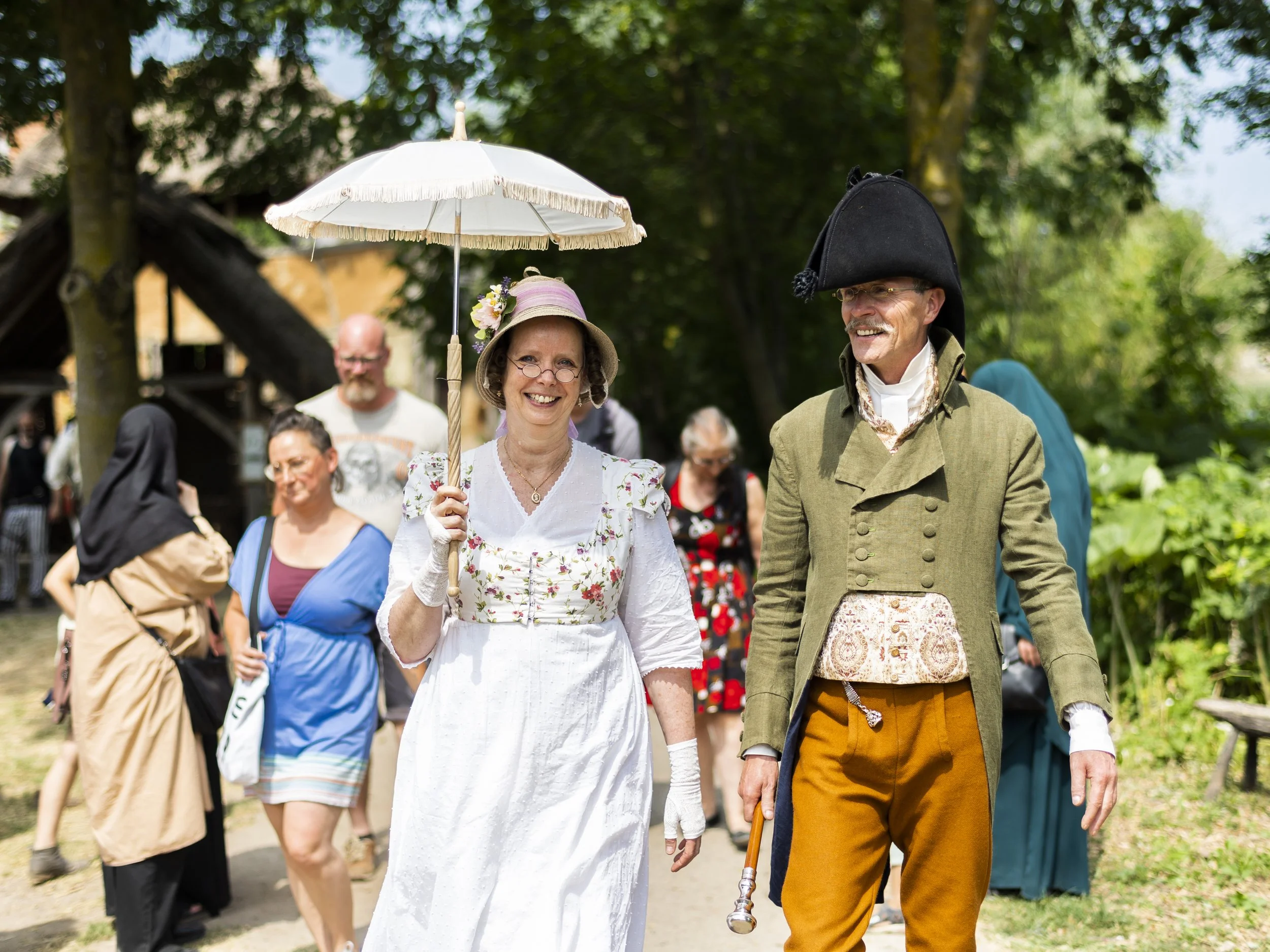 People dressed in historical clothing walking outdoors at a historical reenactment or festival.