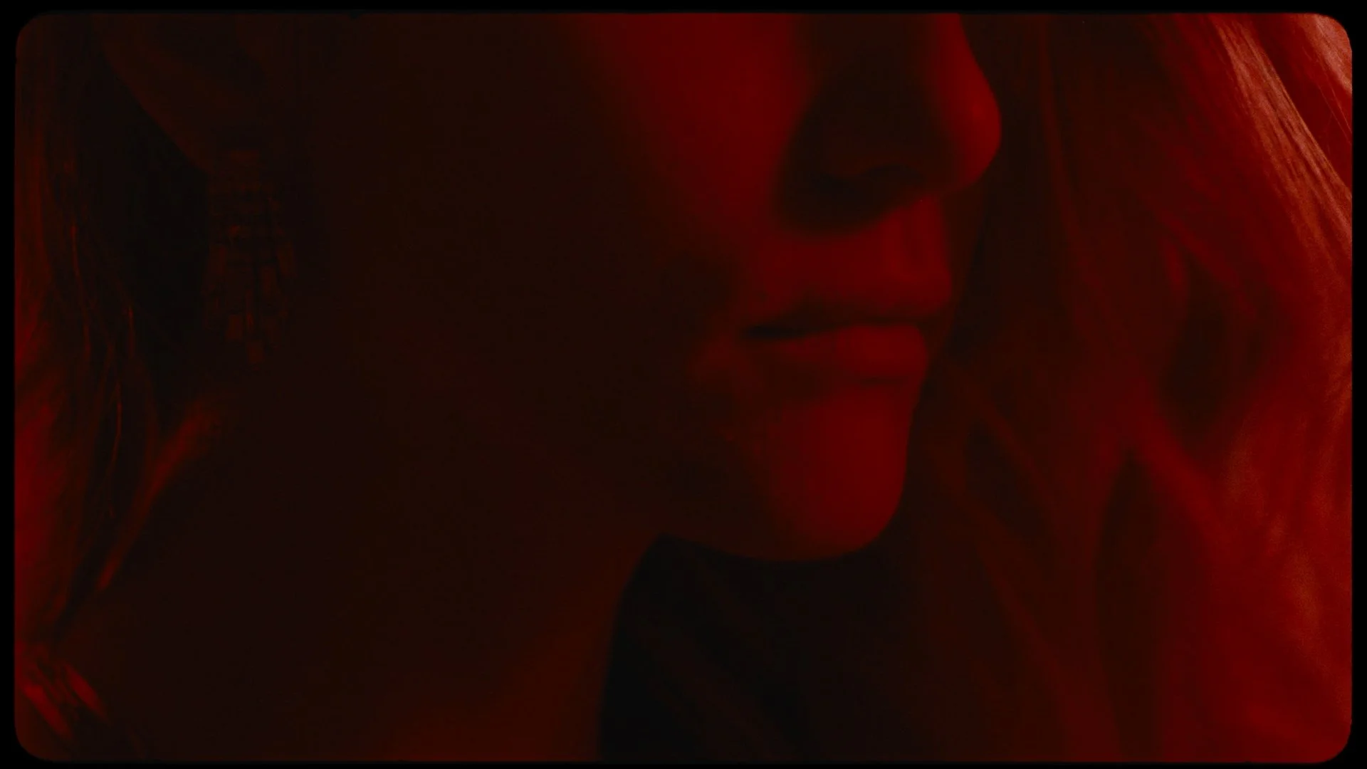 Close-up of a woman's face in red lighting, with her eyes closed and hands resting on her cheek.