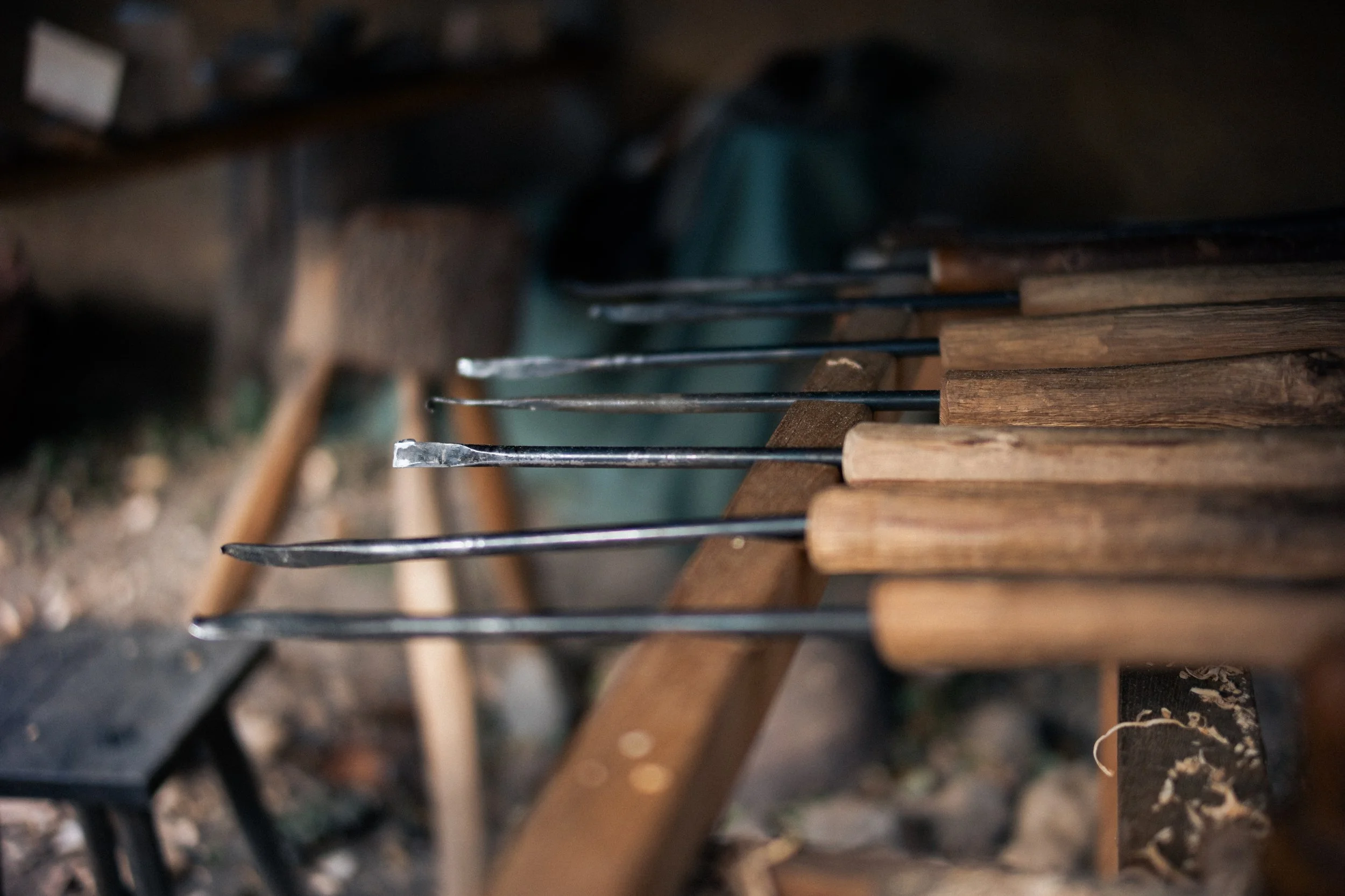 Close-up of a row of small woodworking chisels with wooden handles, resting on a workbench in a woodworking shop.