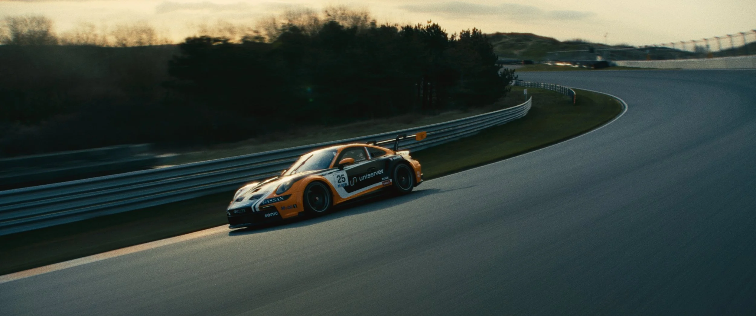 A race car driving on a curving race track with trees and a sunset in the background.