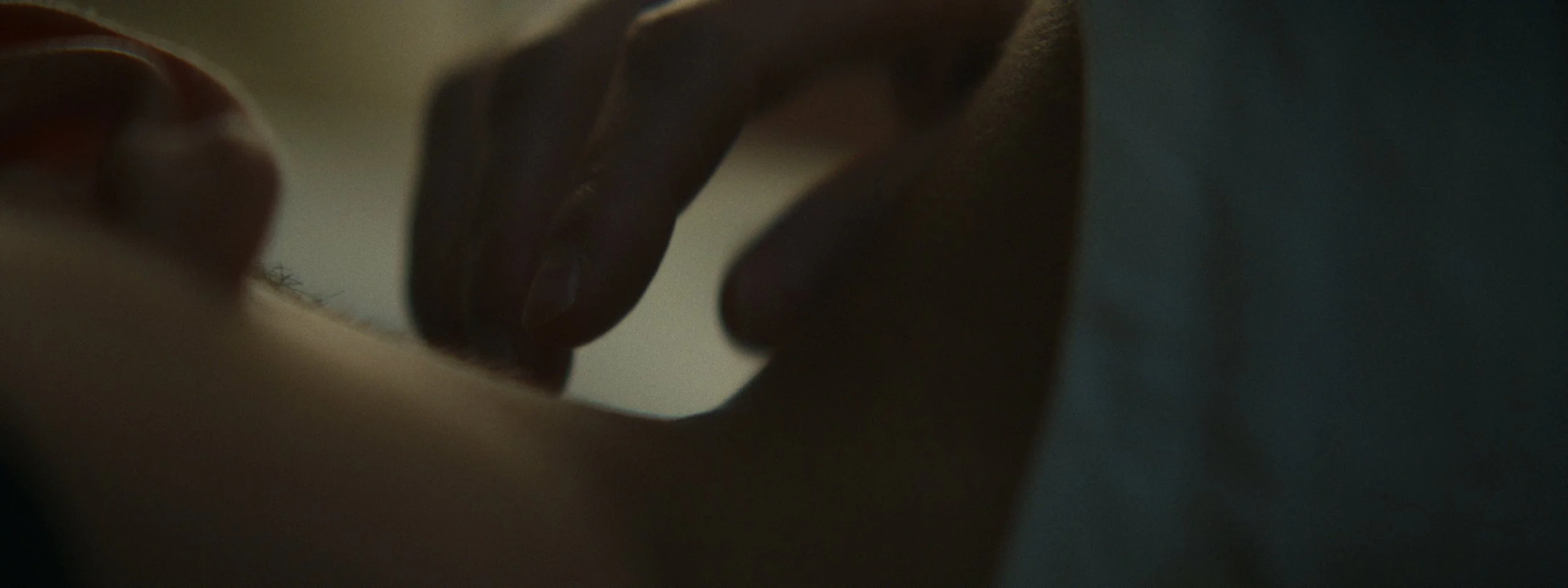 Close-up of a person's hand gently touching or pressing on a surface, with a dimly lit background.