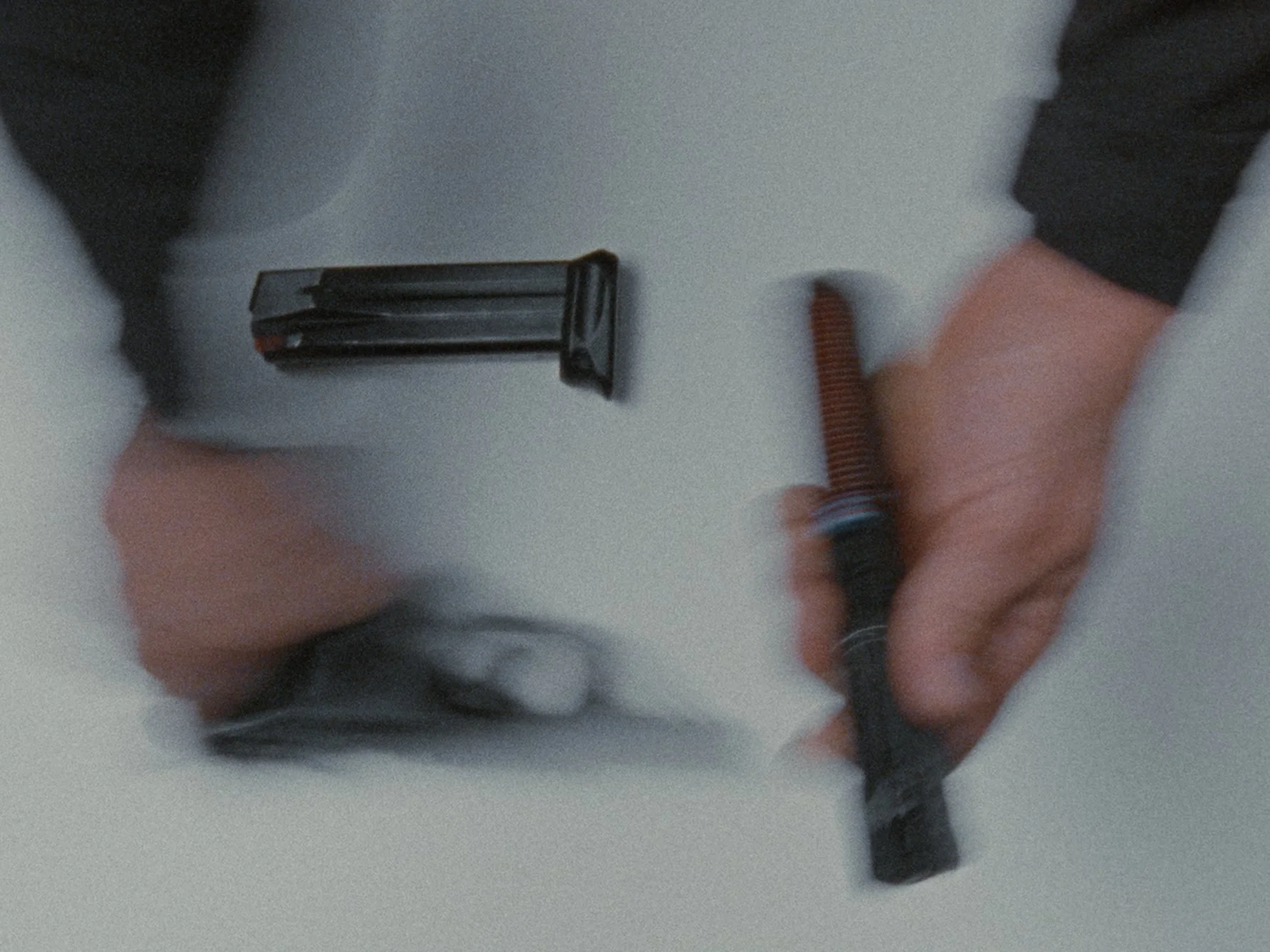 A person holding a magazine and a firearm on a white surface.