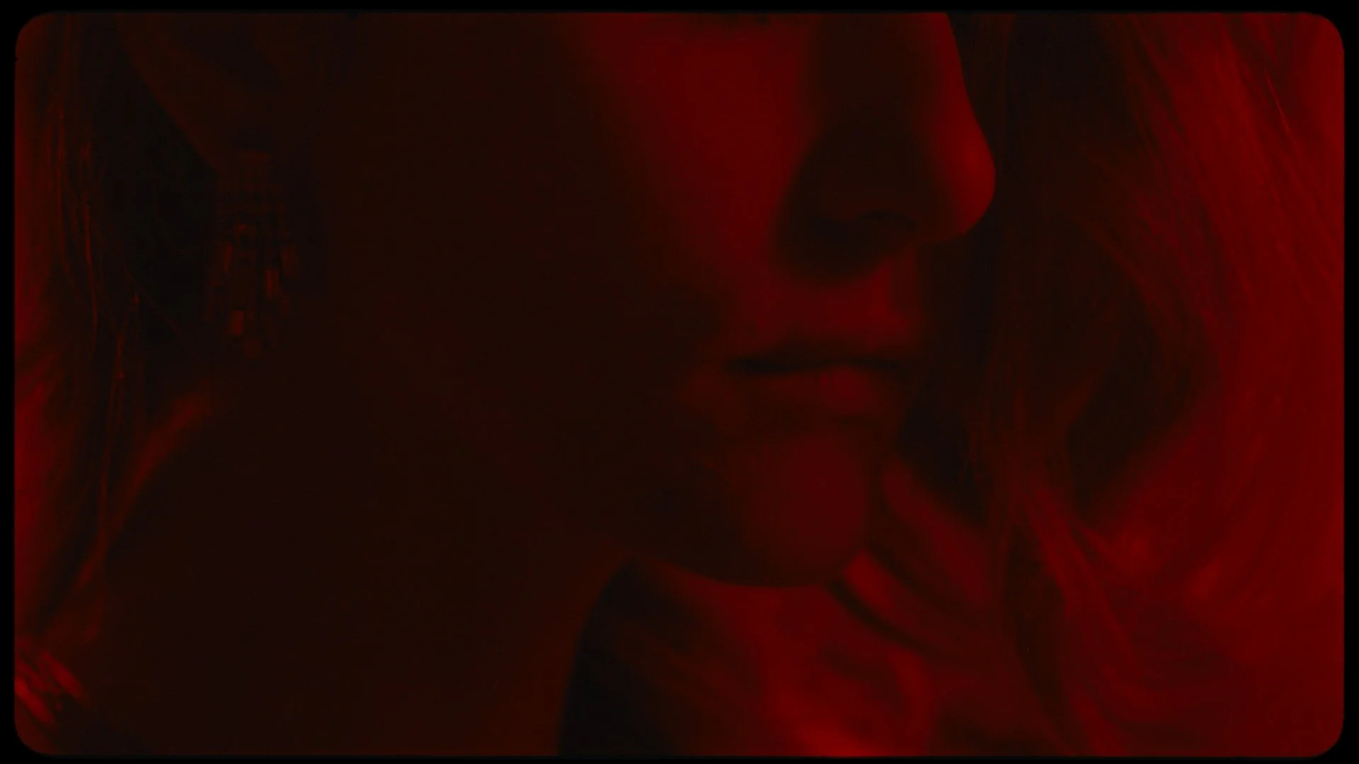 Close-up of a person's face, with a red glow highlighting features, lips slightly parted, and hair visible on the left side.