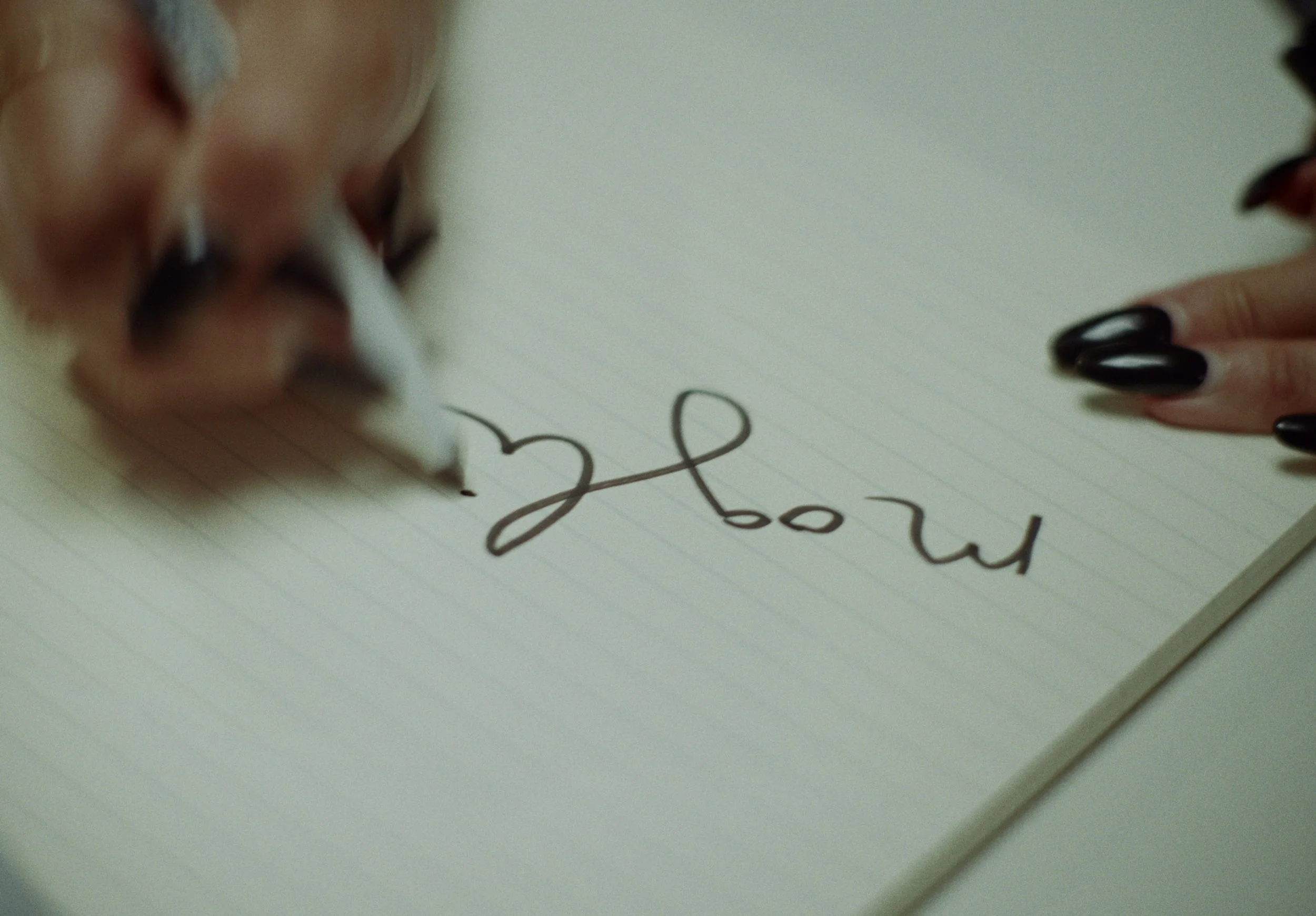 Close-up of a person writing on lined paper with black ink pen, with the word 'happy' partly visible.