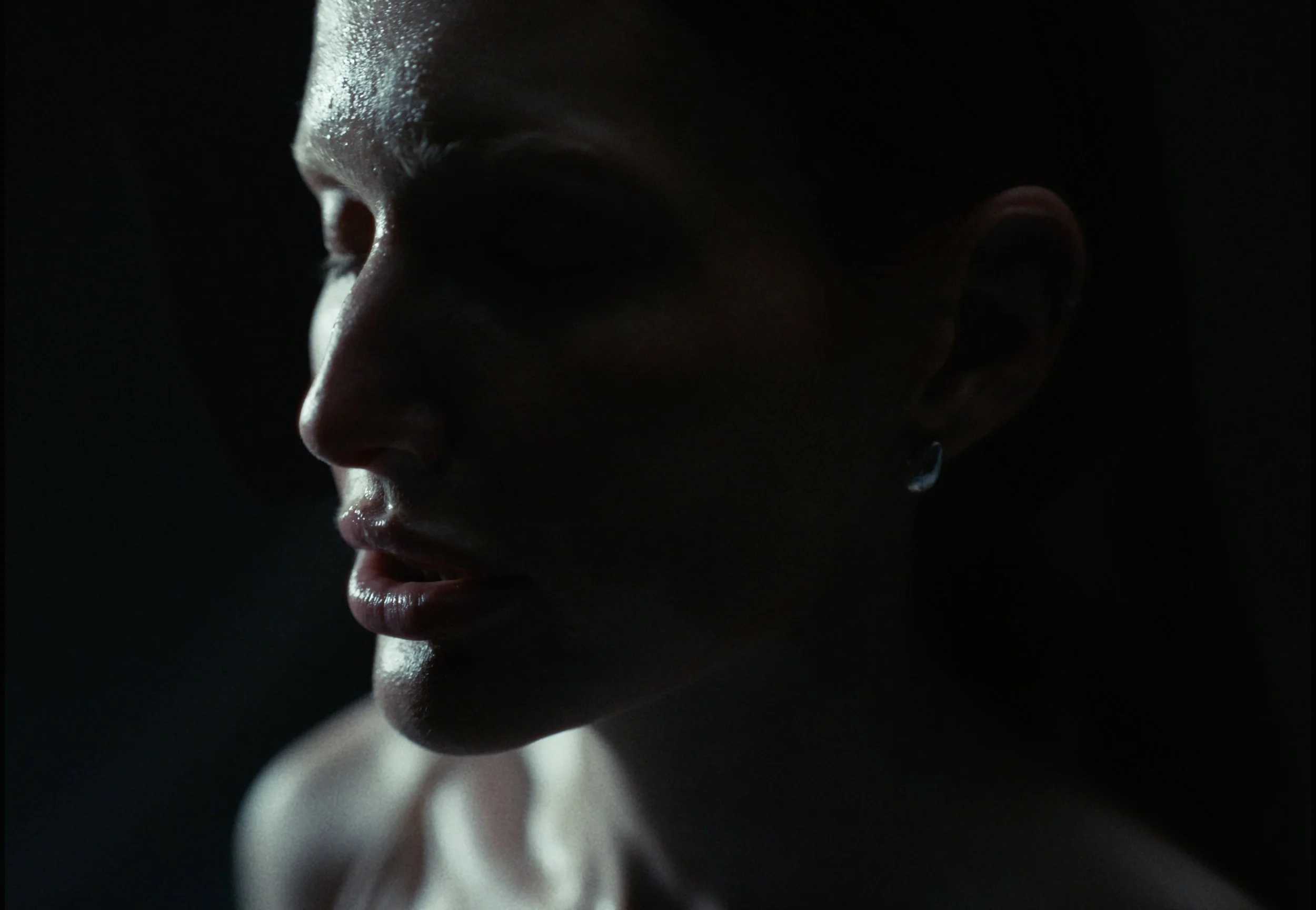 A close-up of a person's face in profile, with dramatic lighting highlighting the features against a dark background.