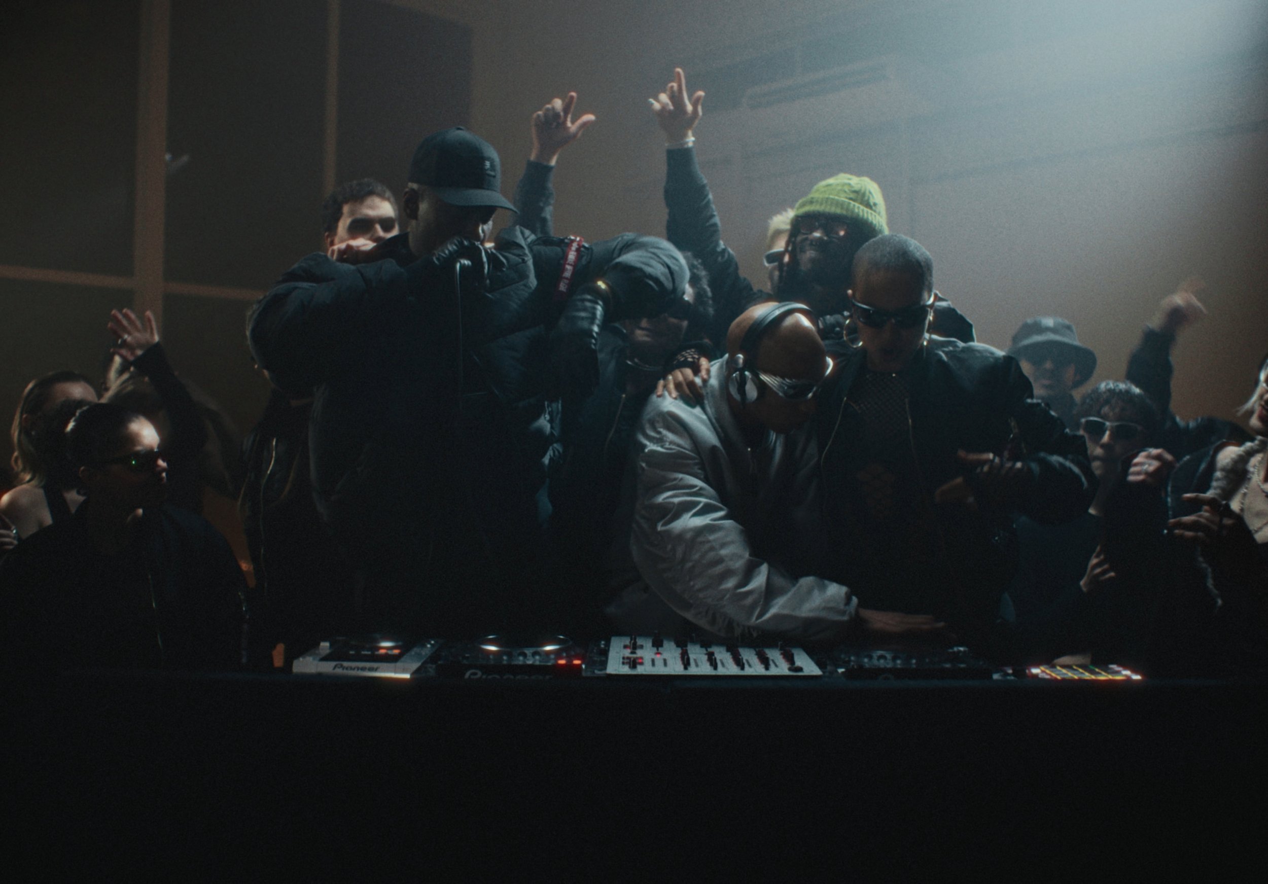 A group of people dancing and socializing in a nightclub or party setting, with a DJ or music equipment in the foreground.