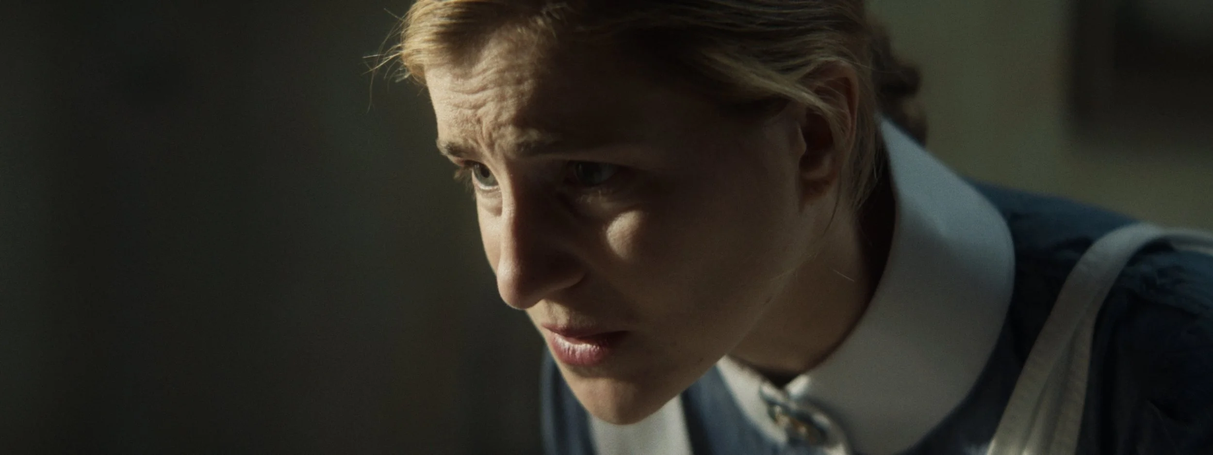 Close-up of a woman wearing a nurse outfit, looking down with a focused expression, on a dark background.