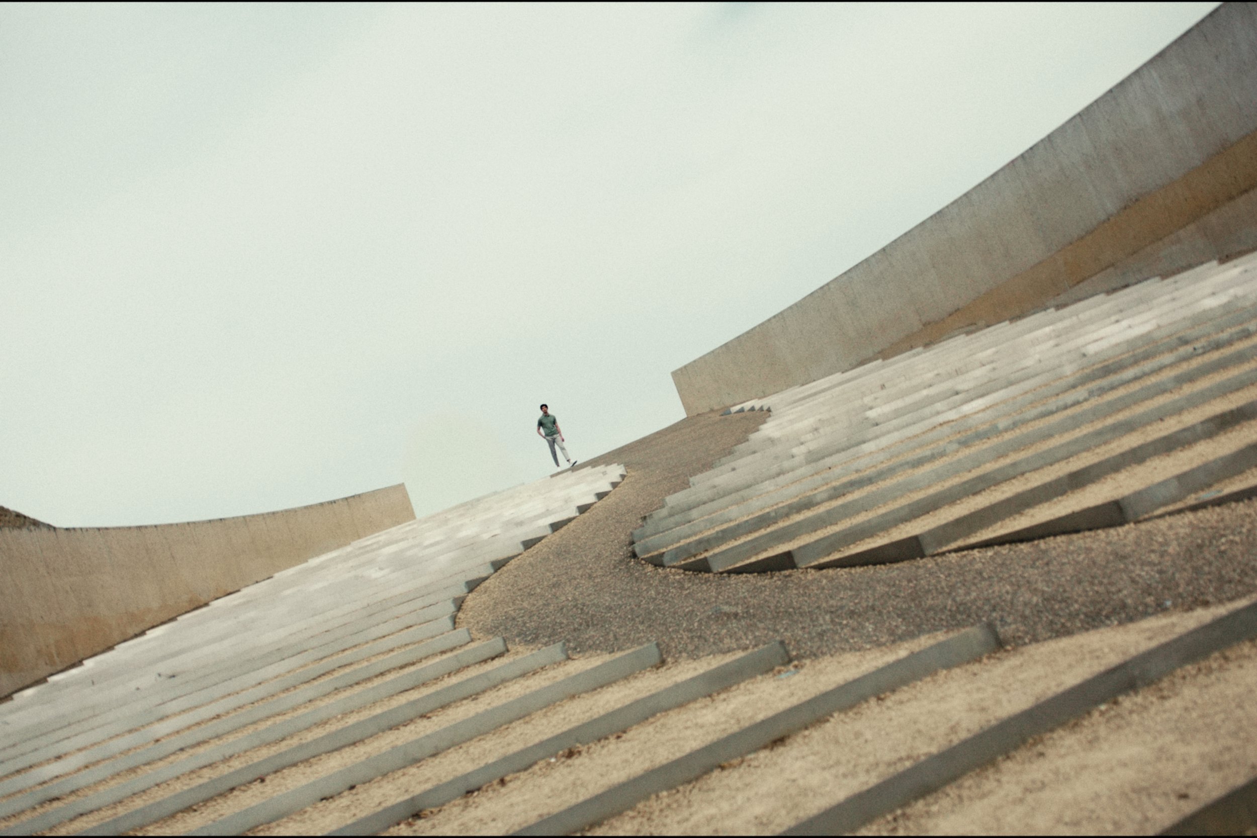 A person walking on a sloped, layered concrete structure outdoors with a clear sky background.