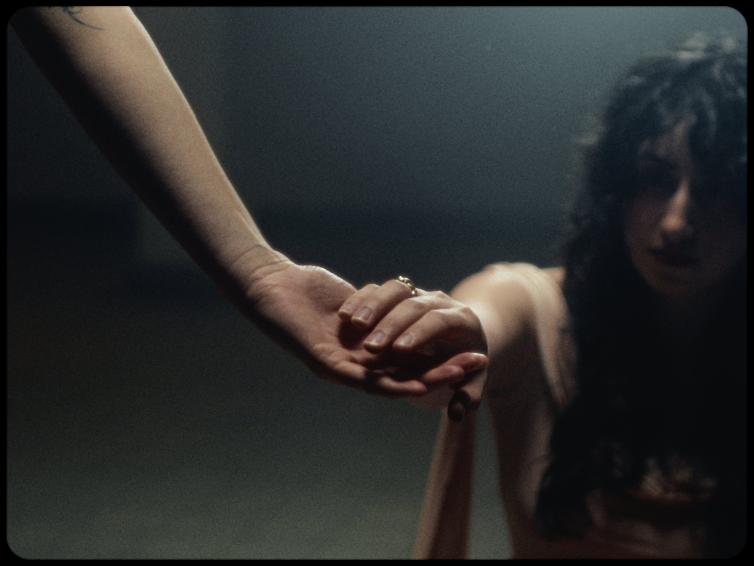 A person with curly hair and a dark shirt holding another person's hand in a close-up shot.