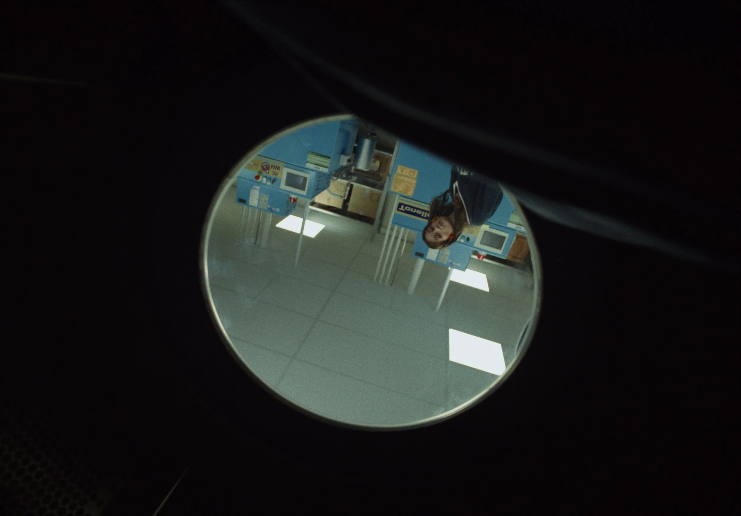 Reflection of a woman at an ATM inside a store, seen through a small round mirror.