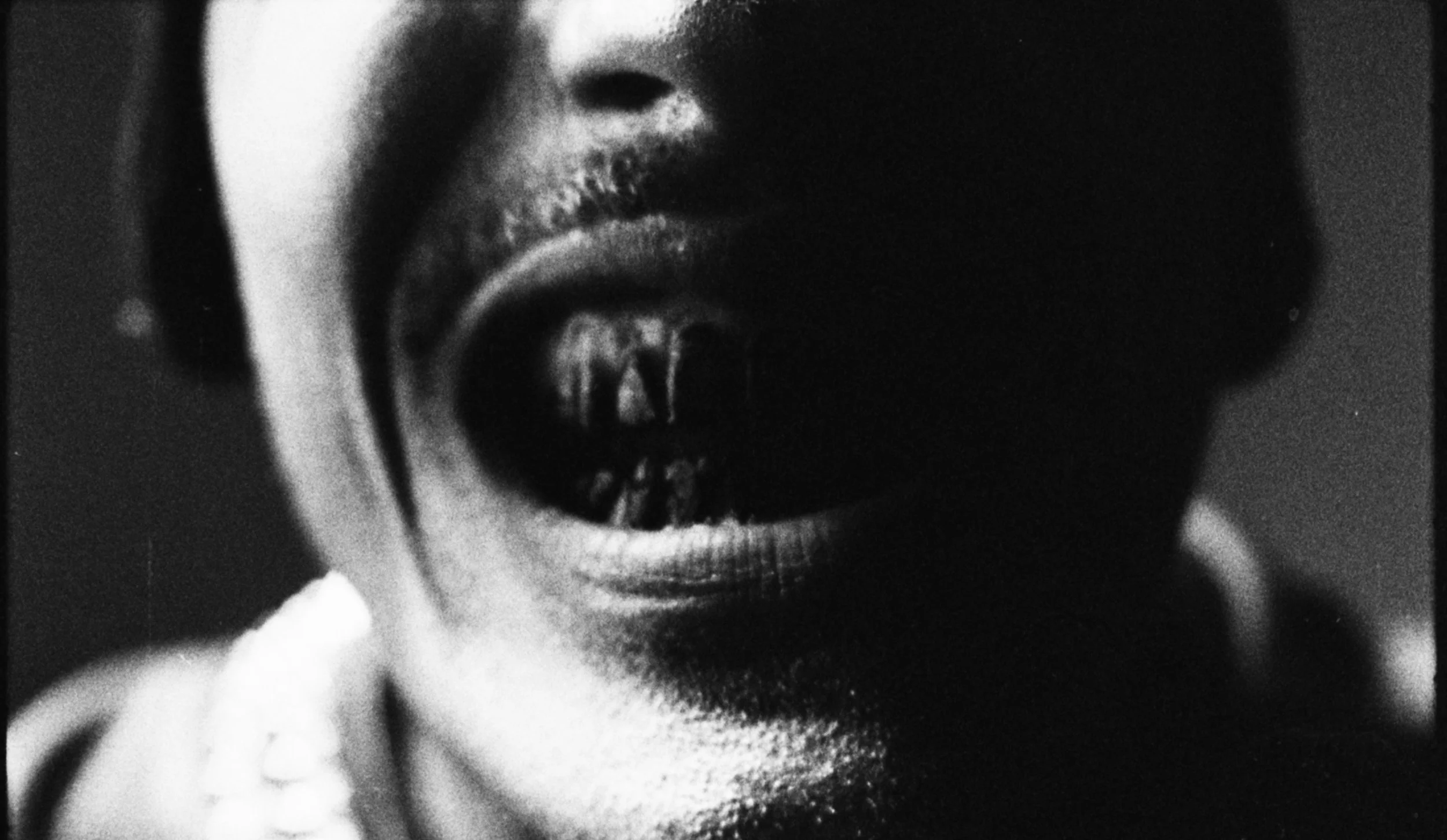 Close-up of a person's face in shadow, with their mouth open, revealing teeth, in black and white.