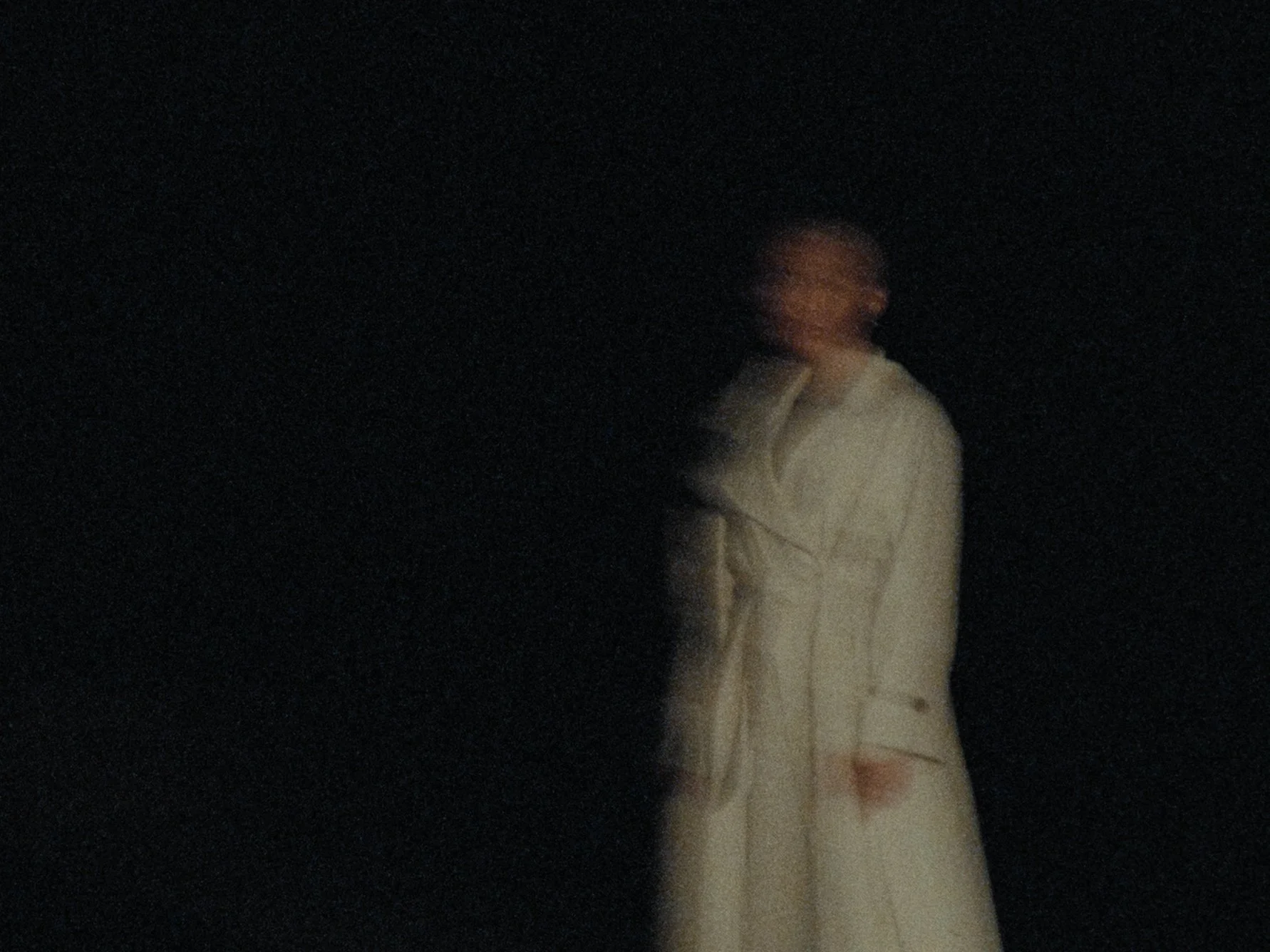 A person with long hair, wearing a white robe, appears to be in motion in a dark environment.