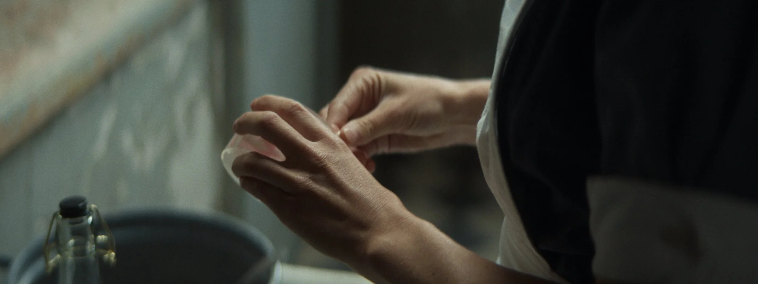 Close-up of a person's hands holding a small white object, possibly a pill or capsule, in a kitchen environment.