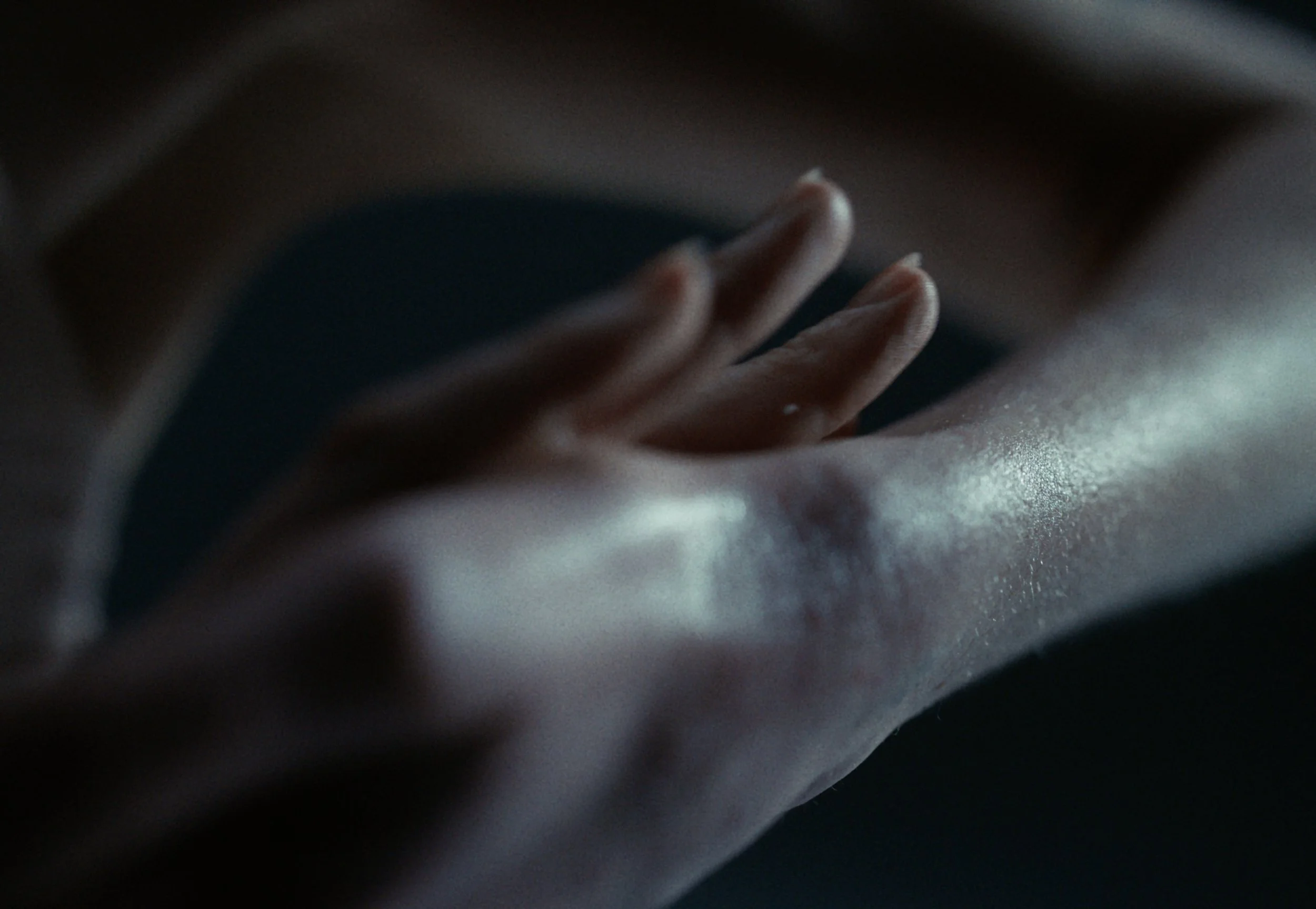 Close-up of a hand with fingers resting on a surface, with dim lighting creating a shadowy atmosphere.
