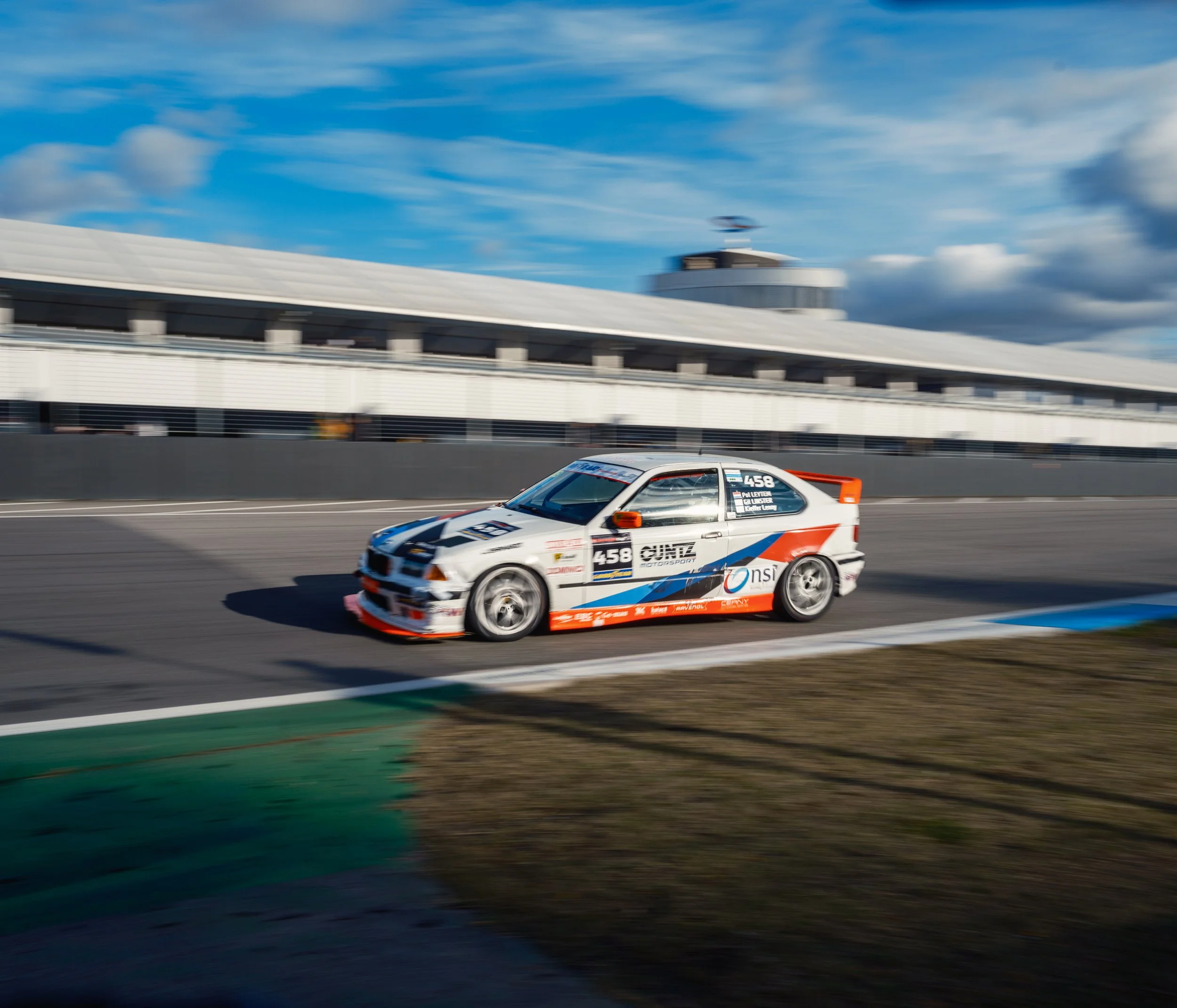 A race car on a race track with a blue sky and clouds in the background.