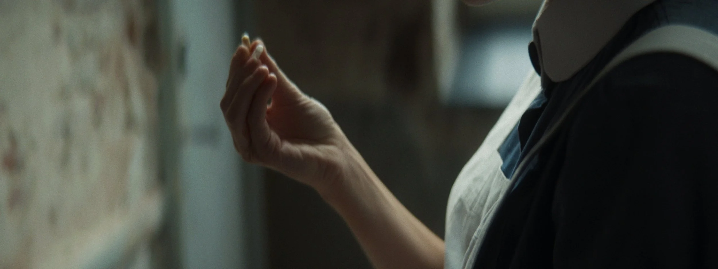 Close-up of a person's hand reaching toward a wall with notes or papers, wearing a white apron and a dark shirt.