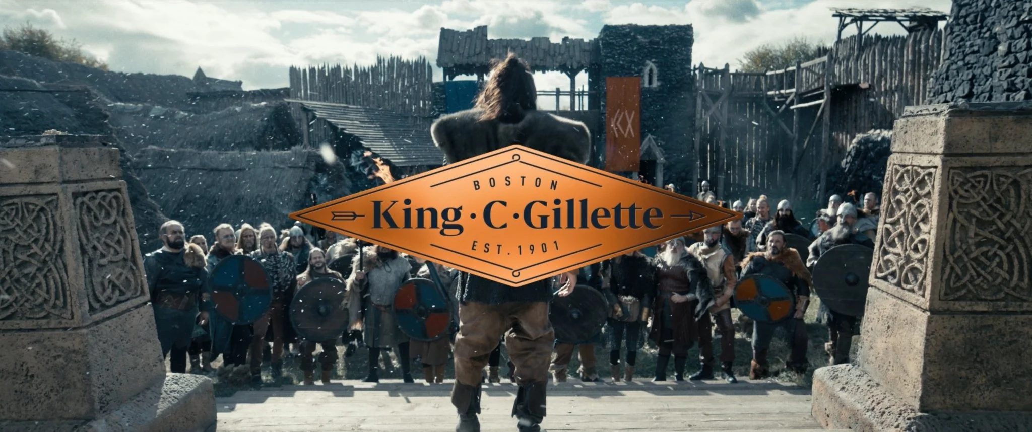 Scene from the TV series 'Vikings: Valhalla' showing Vikings preparing for battle, with a large group of warriors holding shields, and ruins in the background, with the logo of King C. Gillette overlaid.