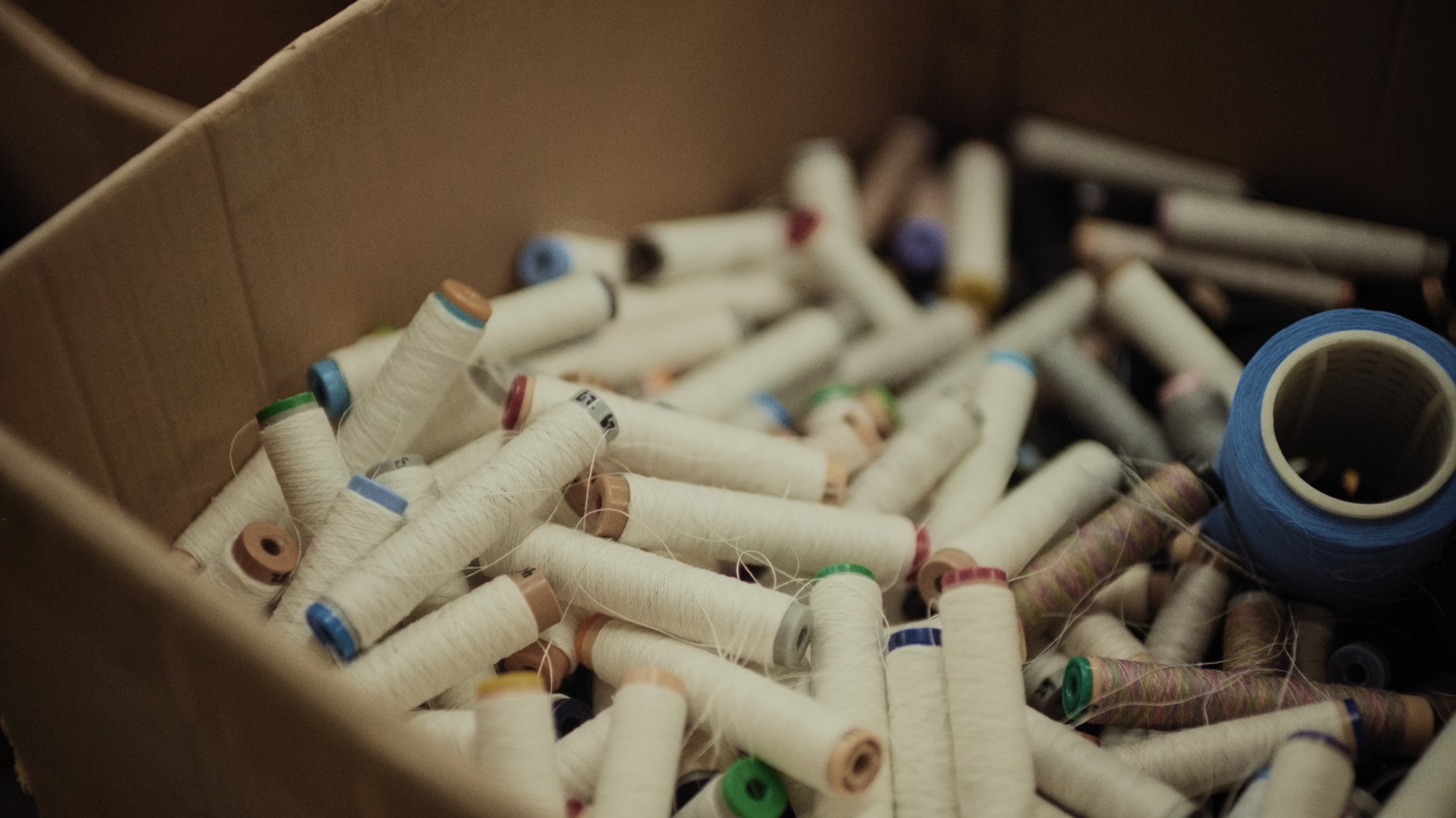 A box filled with numerous spools of white thread with colored caps, along with a roll of blue tape.