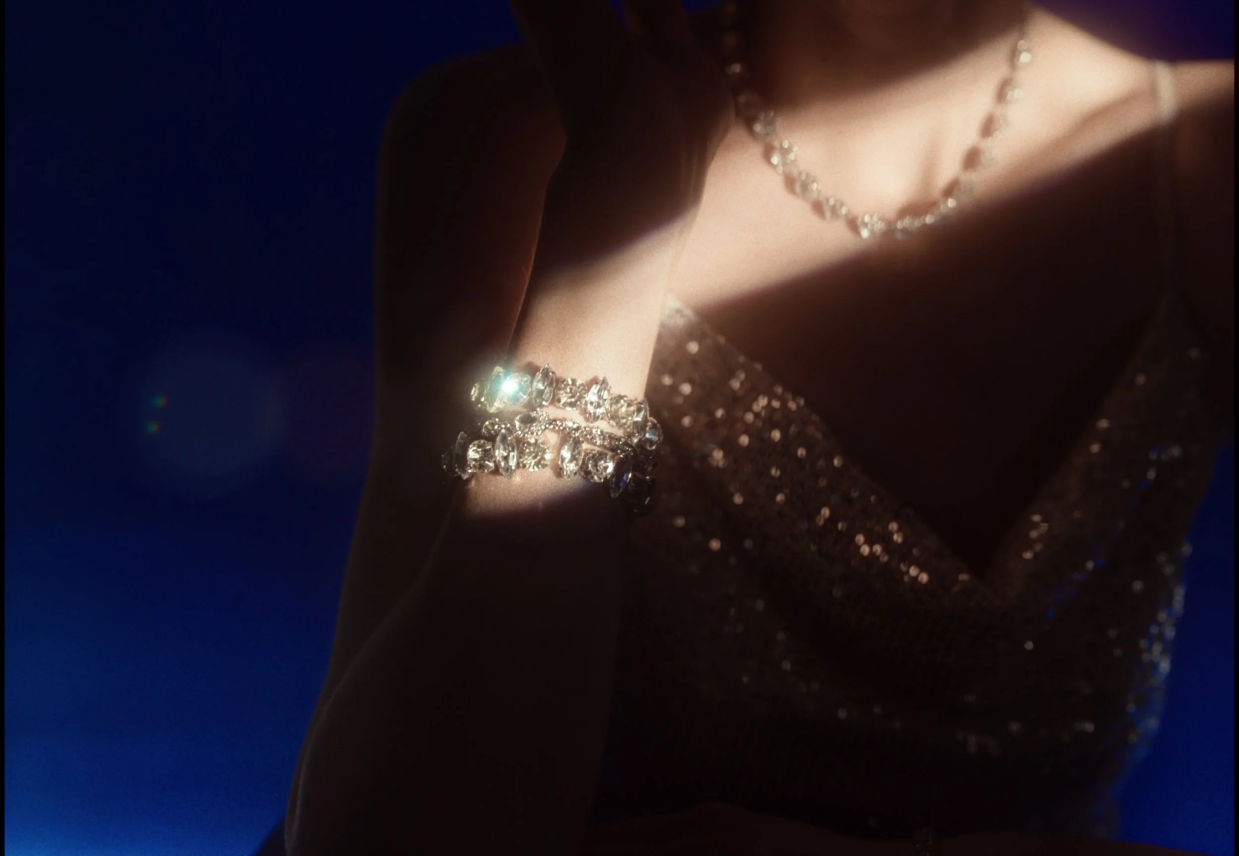 Close-up of a woman wearing a sparkly black dress, a diamond necklace, and a matching bracelet, with a dark background.