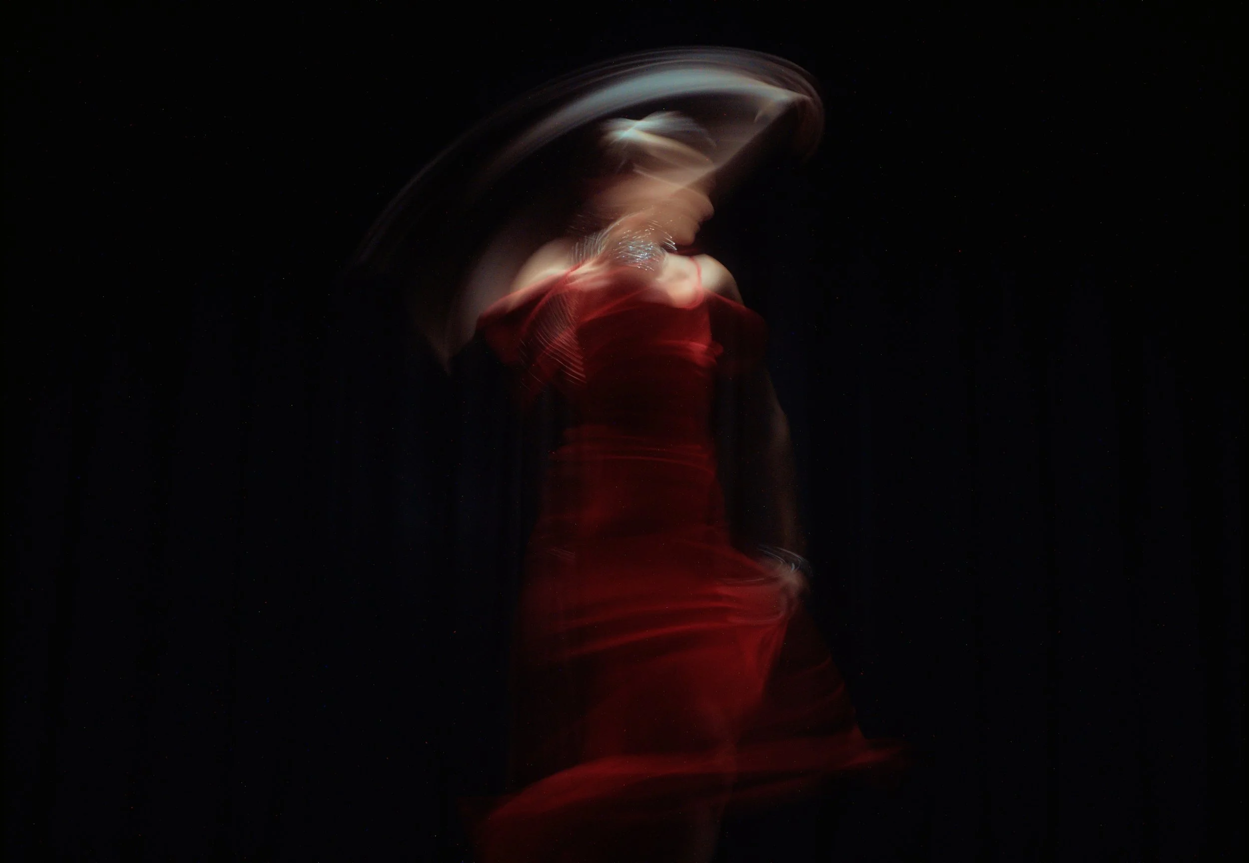 A person in a red dress moving in a dark space with light trails creating a motion effect.