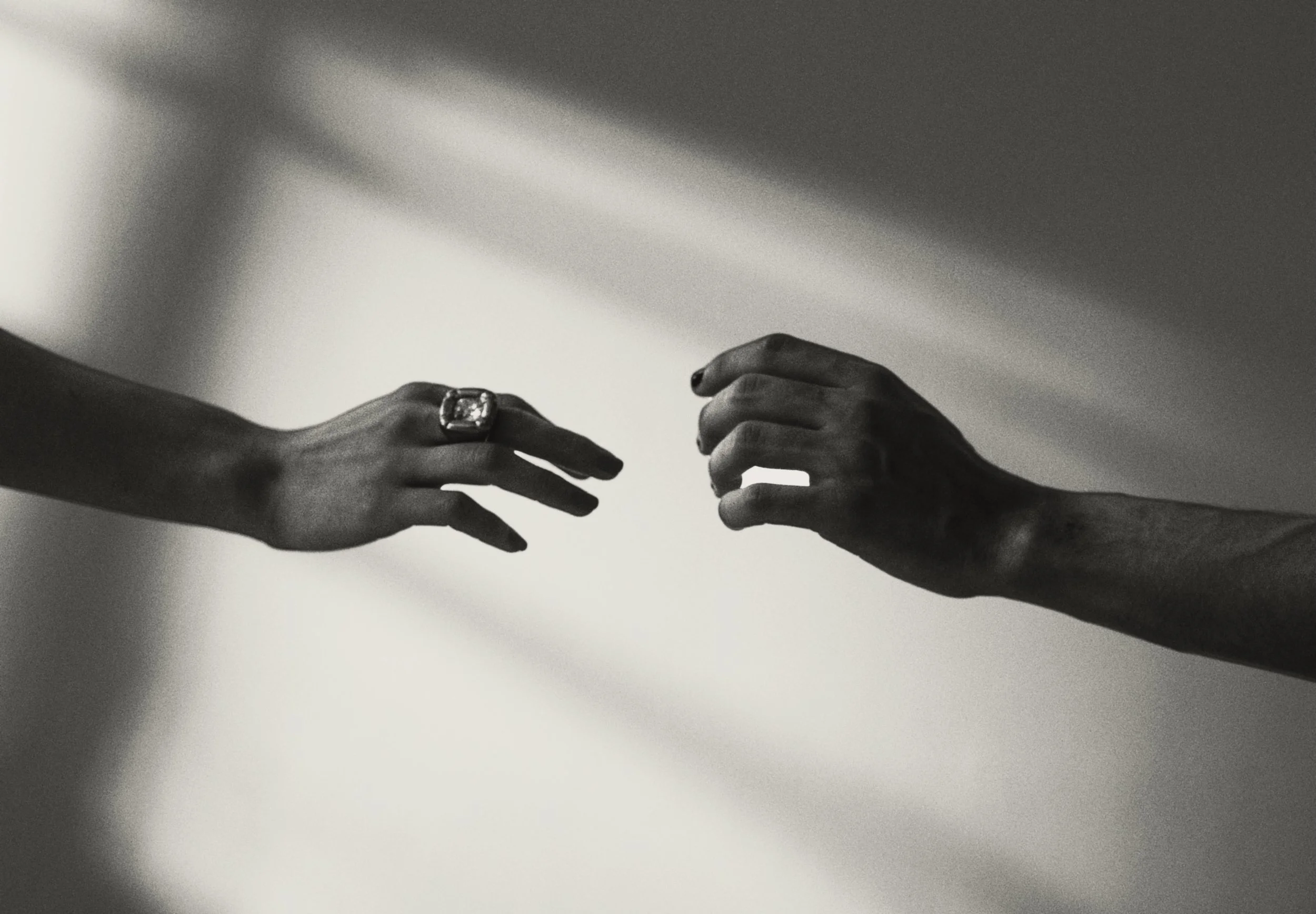 Black and white photo of two hands reaching towards each other, with one hand wearing a large ring.