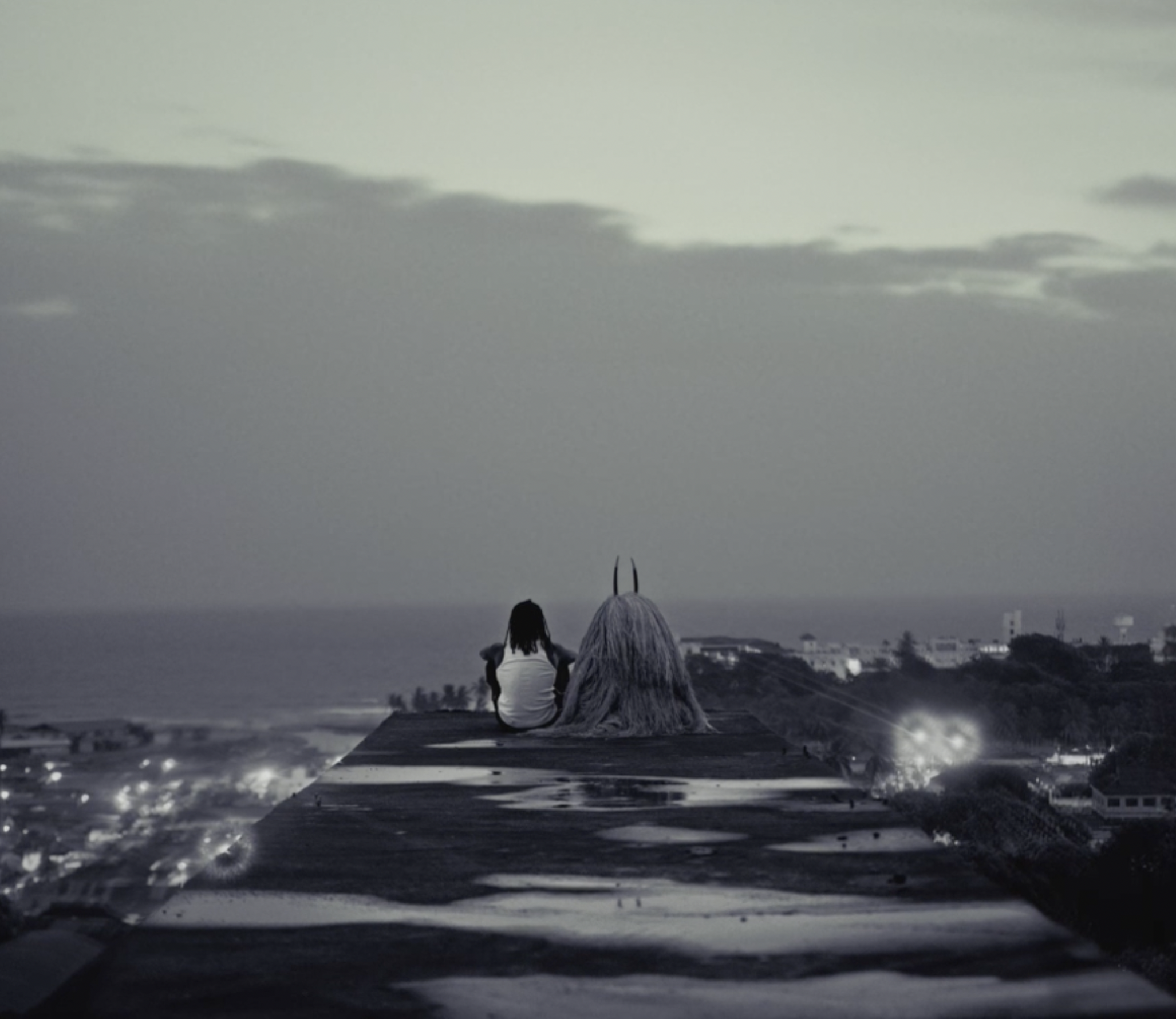 Two women sitting on a rooftop at sunset, watching the city skyline and enjoying the view.