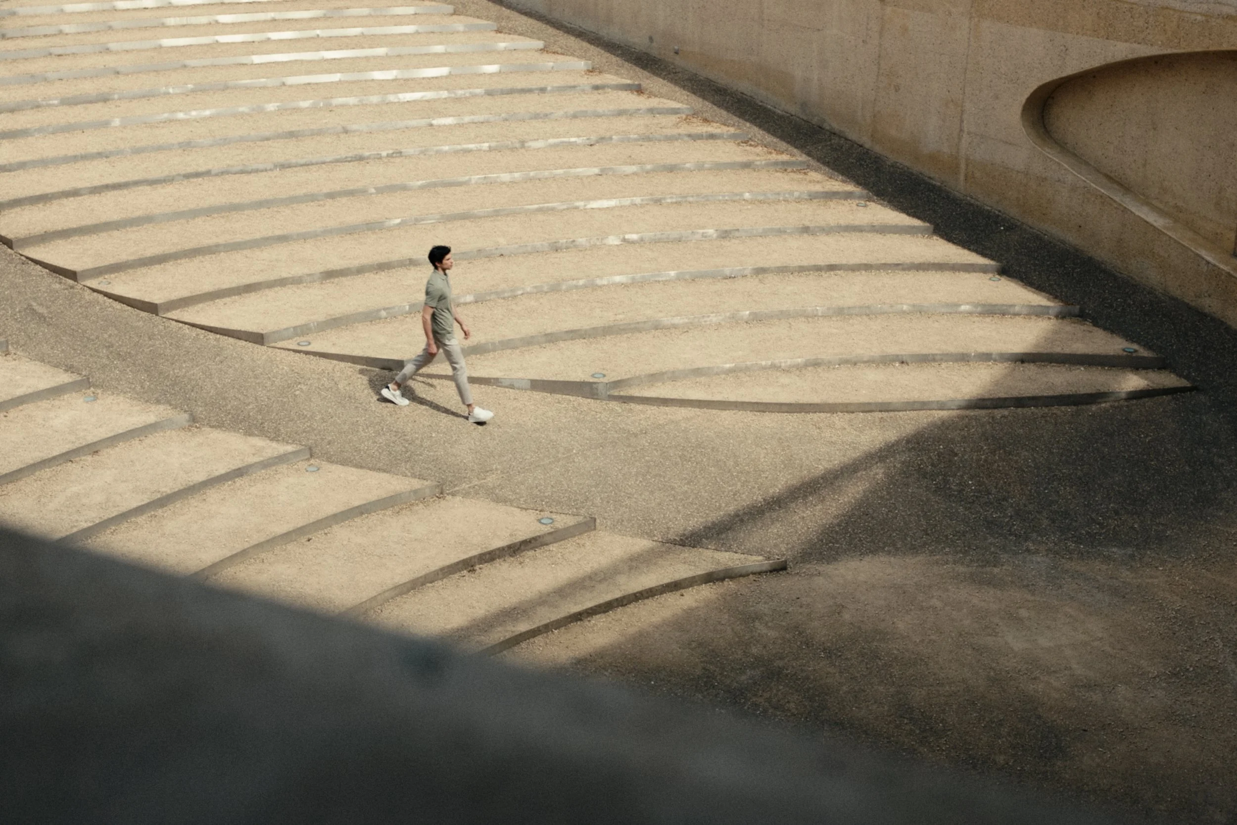 A person walking on a set of outdoor stairs with a sandy surface, adjacent to a concrete wall.