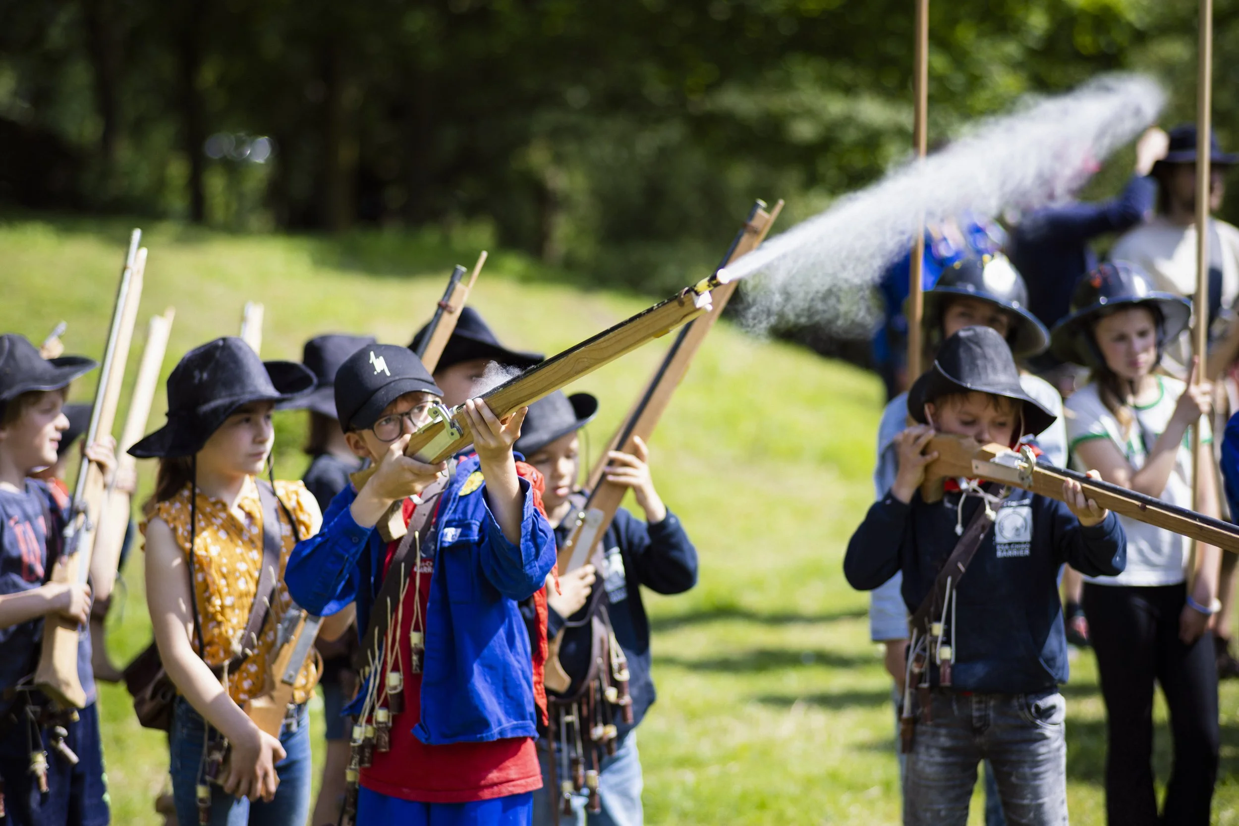 Children dressed as historical soldiers, holding toy rifles, participating in a reenactment or educational activity outdoors on a sunny day.