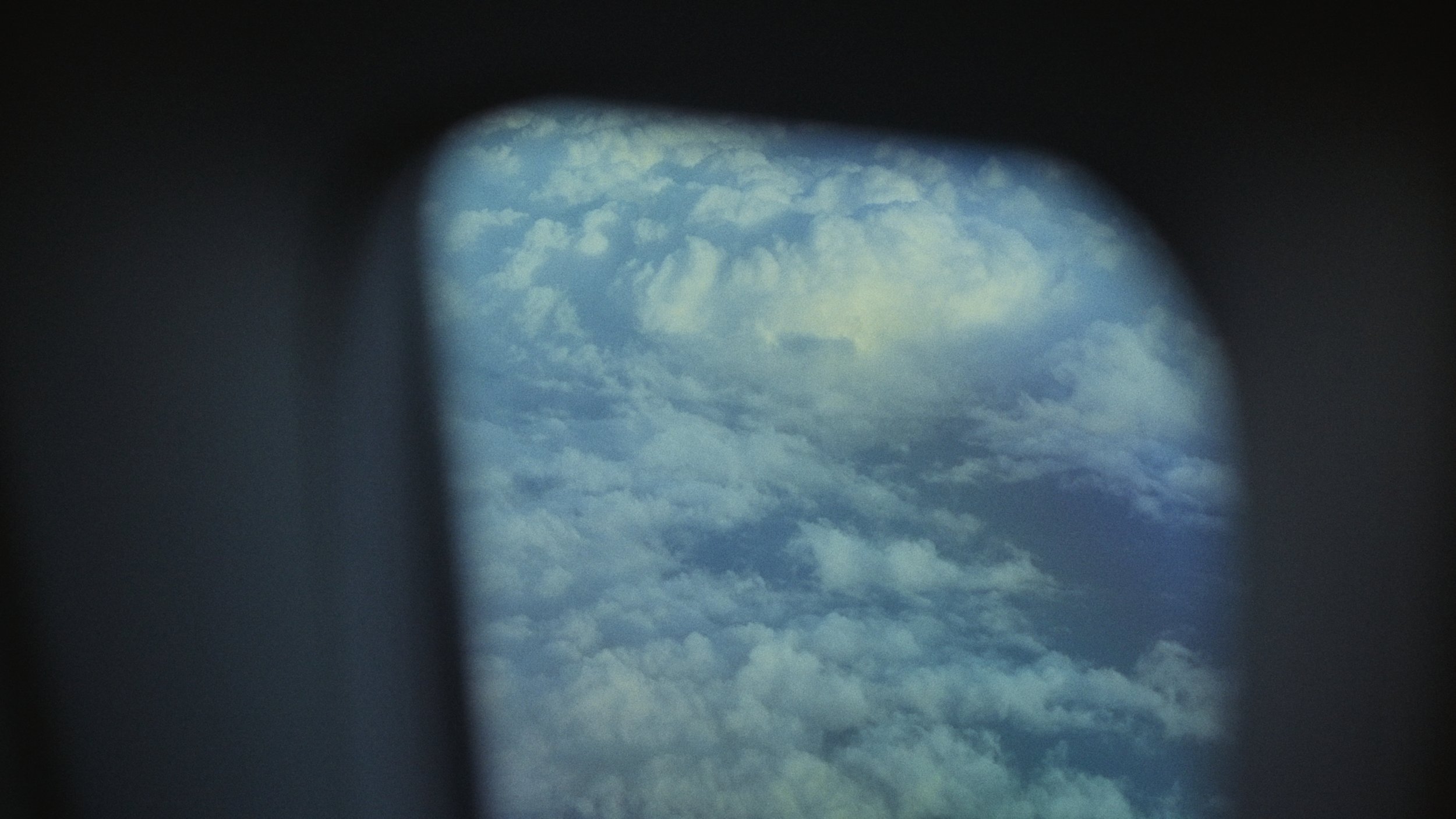 View of a cloudy sky through a circular opening or window, with dark edges surrounding the scene.