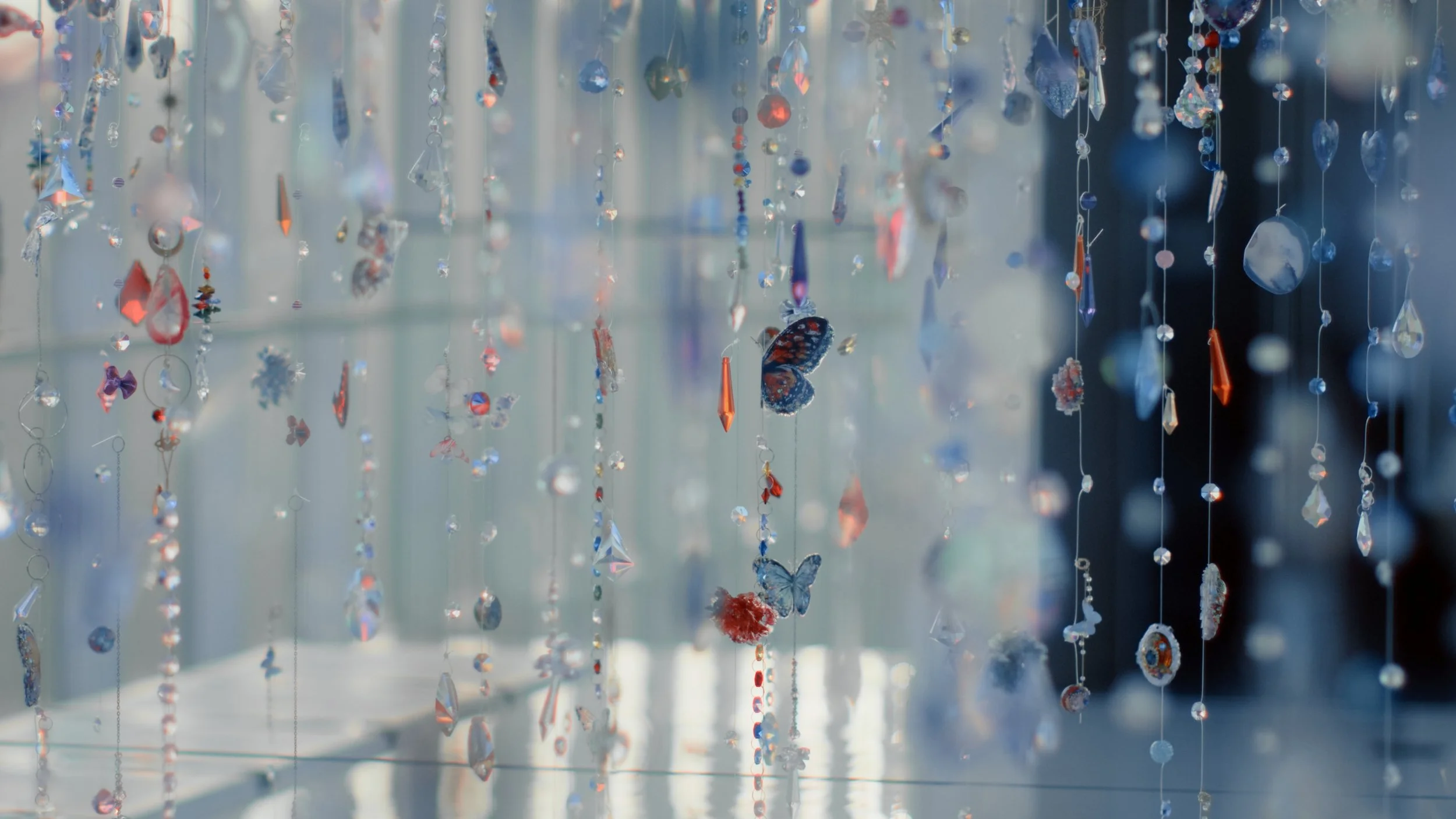 Close-up of hanging crystal and glass ornaments, including butterflies, hearts, spheres, and geometric shapes, reflecting light and creating a sparkling display.
