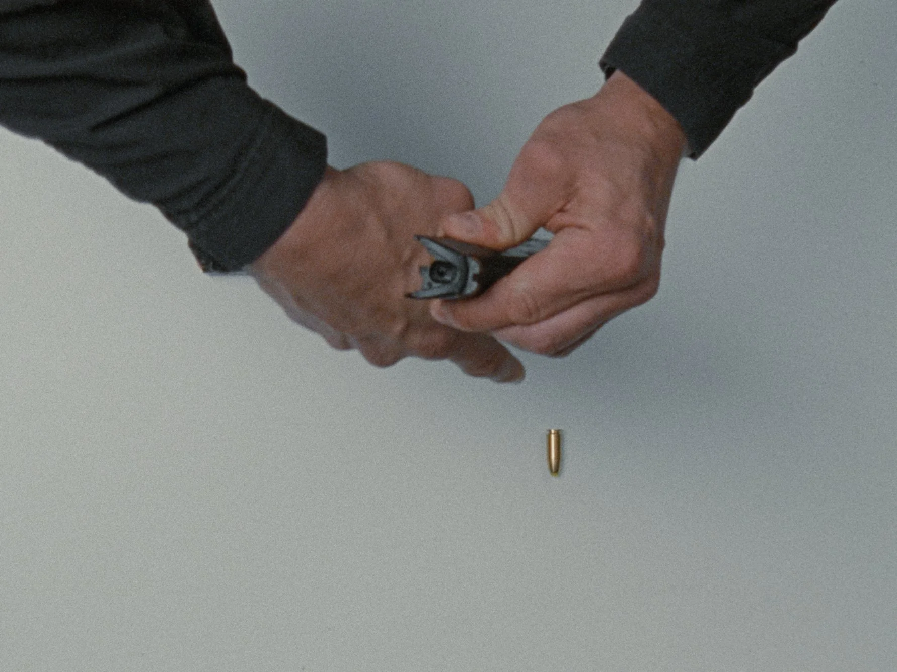 Two people shaking hands above a table with a bullet sitting on it, one person is wearing a black long sleeve shirt, and the other has a brown skin tone.