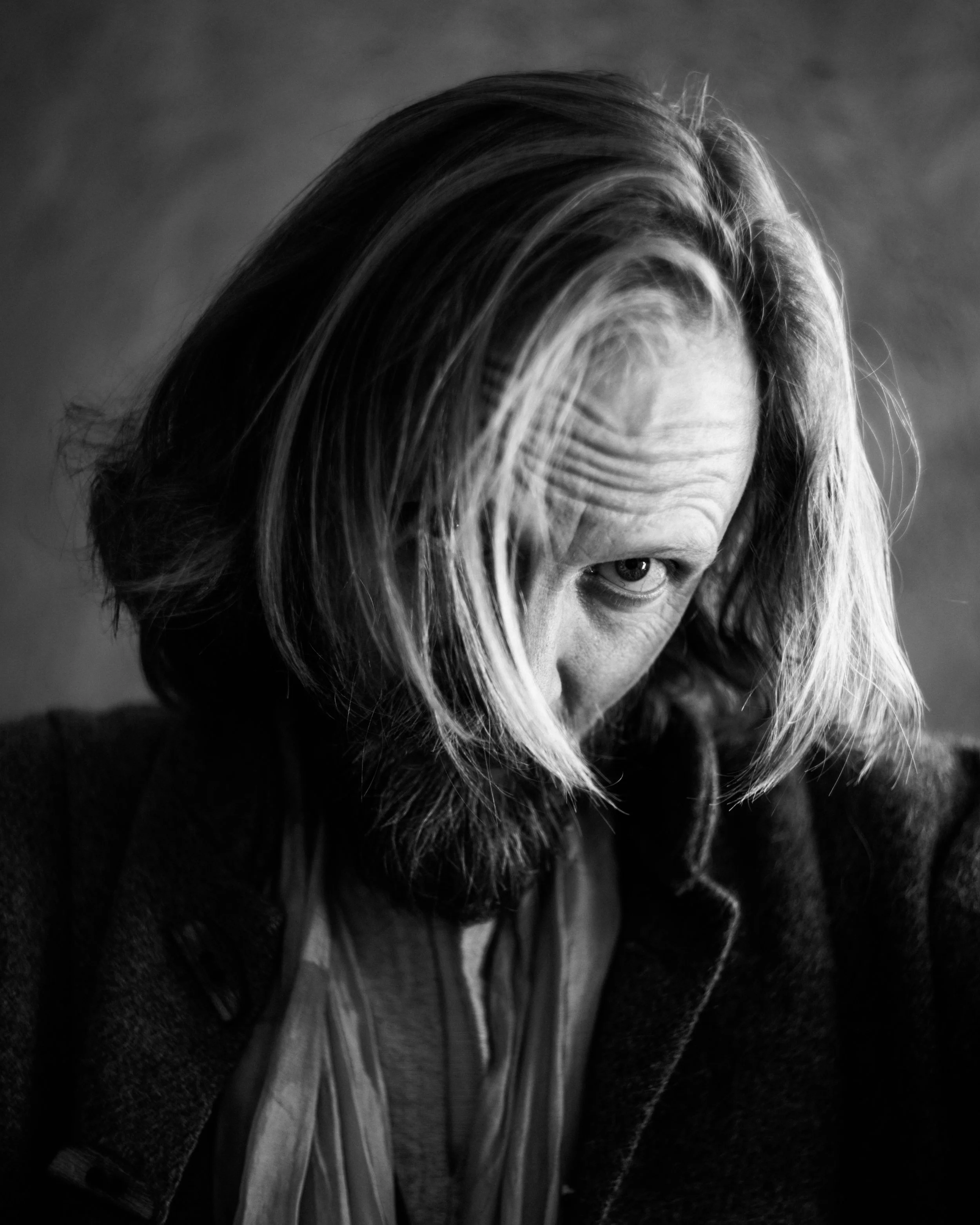 Black and white close-up photo of a person's face, with long hair partially covering the face and one eye visible, looking sideways.