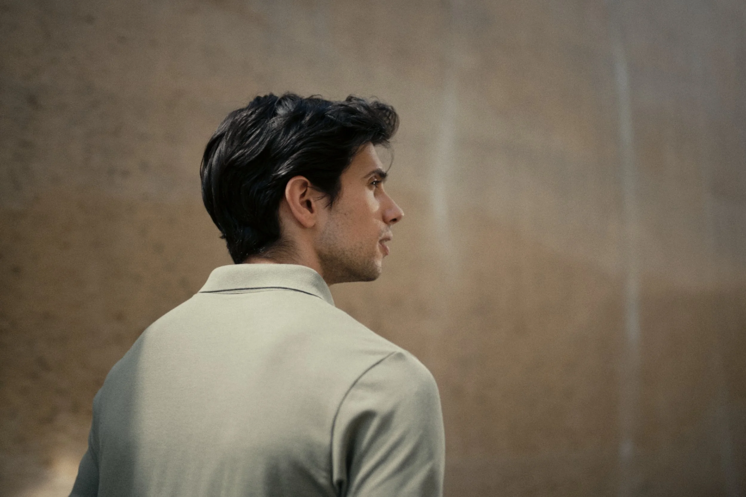 Side profile of a man with dark hair wearing a light-colored shirt, against a neutral background.