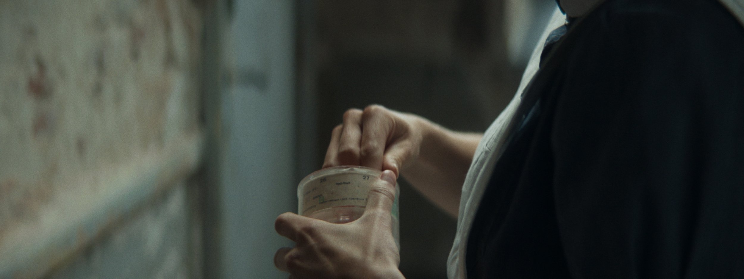 A person holding and opening a small container of pills or tablets with a faded background.