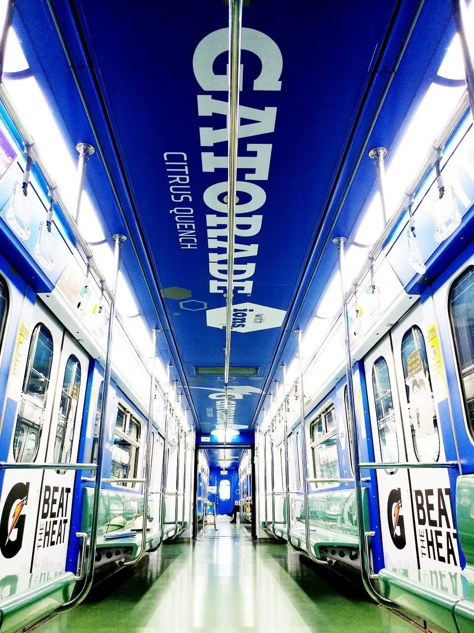 Empty subway train car with blue walls, green seats, and advertisements for Gatorade on the sides, with overhead signage for attractions in Singapore.
