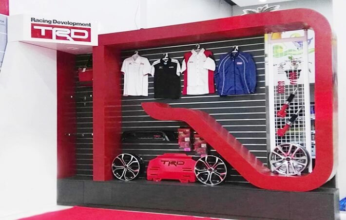 Display shelf with racing-related merchandise, including polo shirts, wheels, and car accessories, with a red and black color scheme and a 'Racing Development TRD' sign.