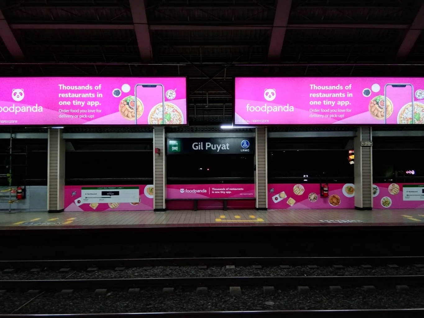 Bright pink Foodpanda advertisements on train station wall promoting ordering food from numerous restaurants via app, with displaying food images and a phone.