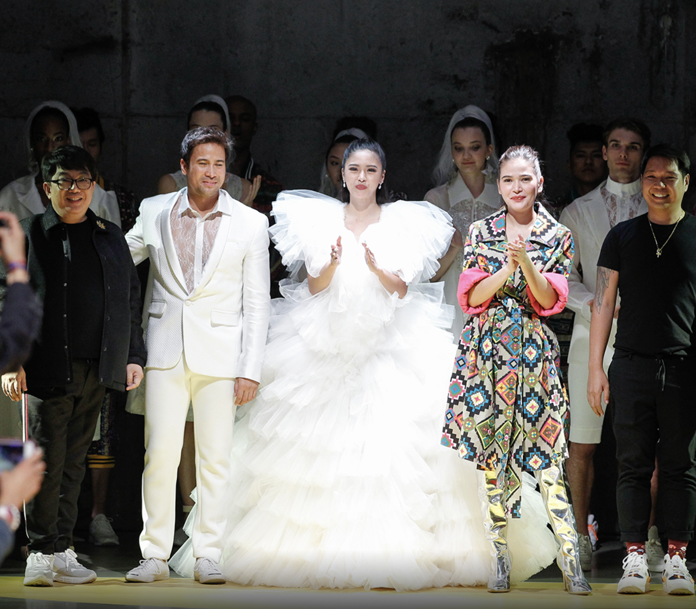 Filipinoe celebrities including Sam Milby, Bella Padilla, and Kim Chiu, including a bride in a white wedding gown, standing with a man in a white suit, a woman in colorful patterned clothing, and others in various outfits, some clapping and smiling.