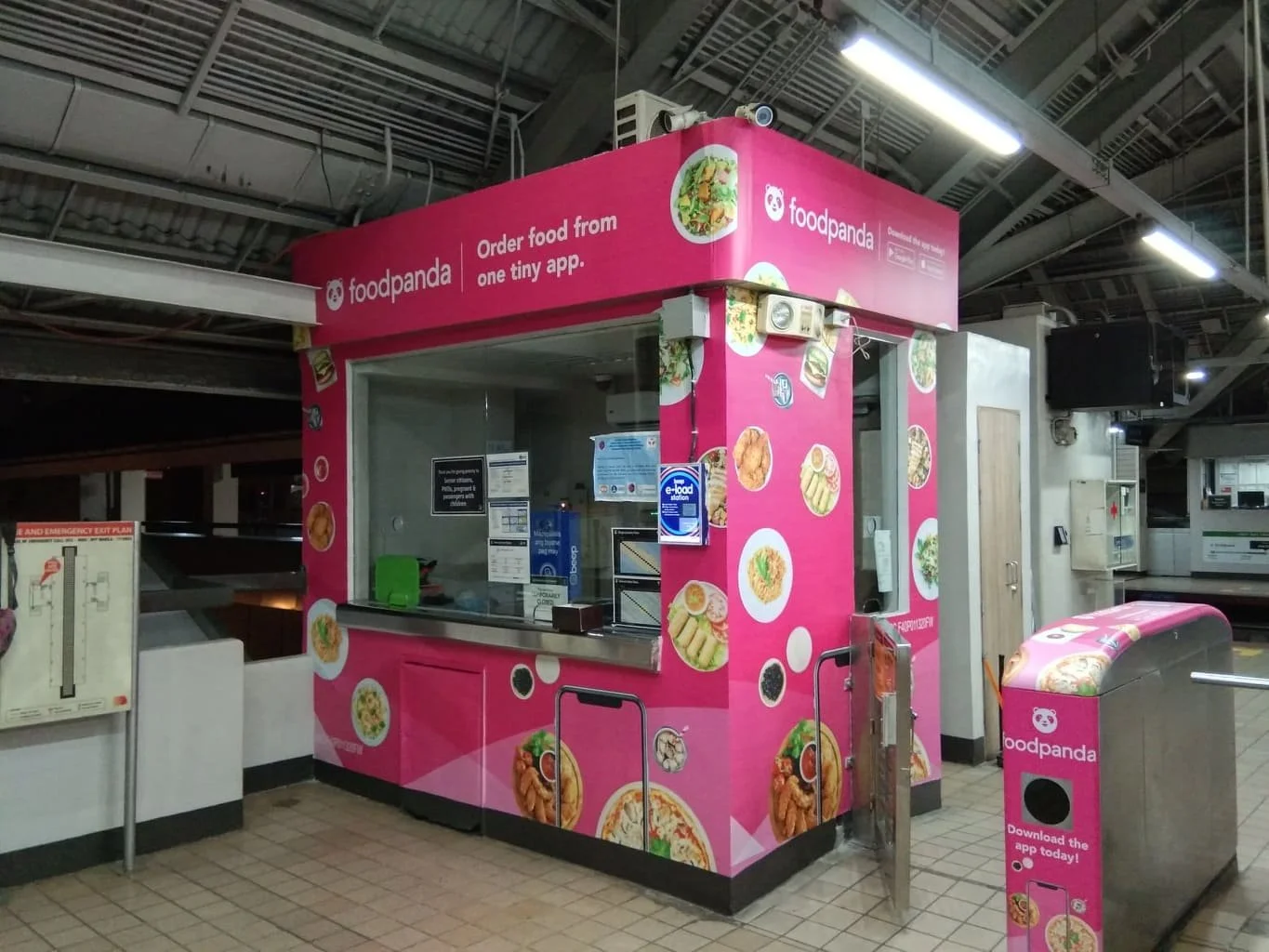Pink Foodpanda food stall inside a building, decorated with images of various dishes, with a small counter and a container for orders.
